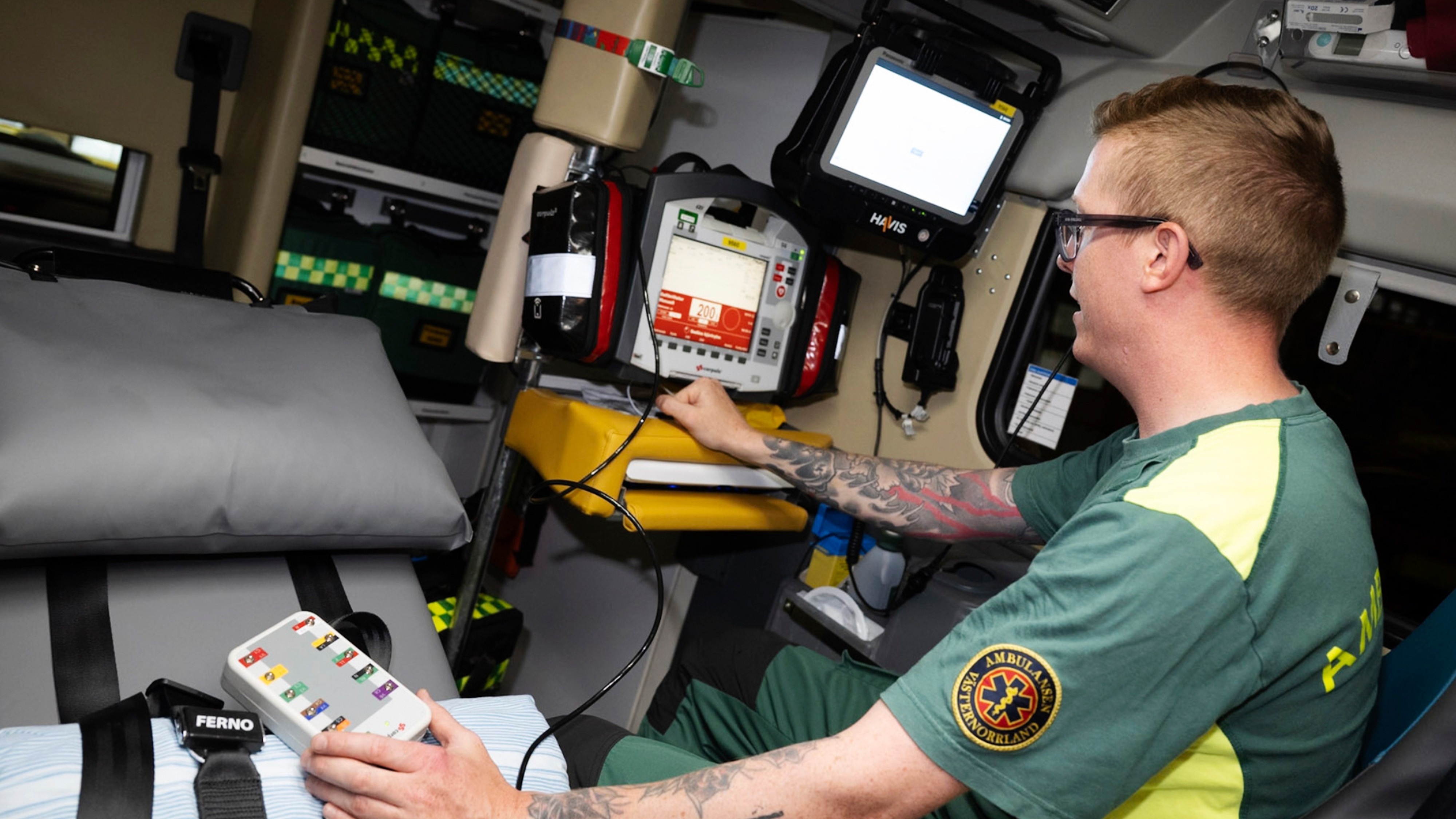 En ambulanssjukvårdare använder medicinsk utrustning i en ambulans, tittar på en skärm och håller ett kontrollpanel.