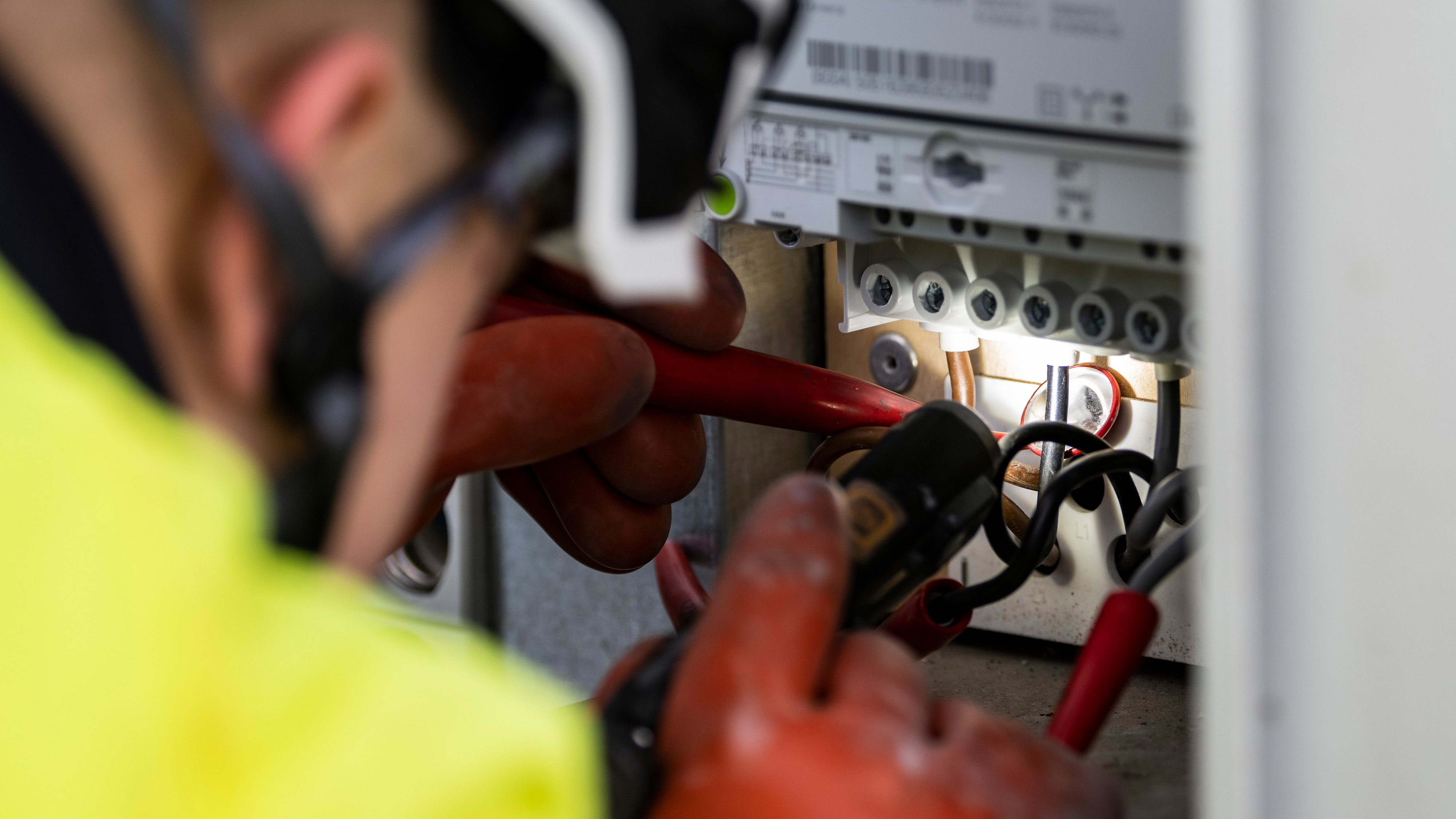 En arbetare med skyddshandskar och skyddsutrustning använder verktyg för att arbeta med elledningar i en panel.