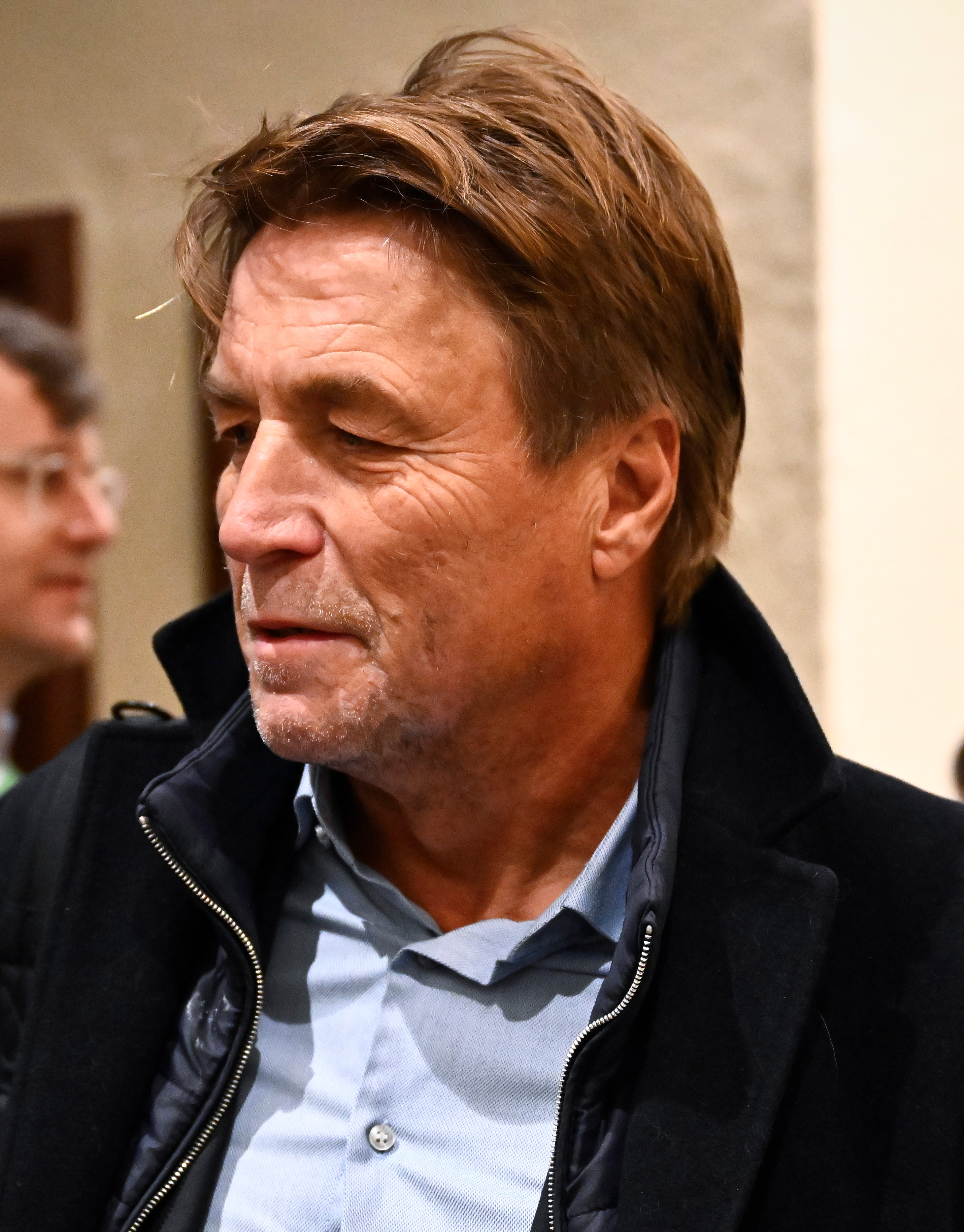 Thomas Bodström i blå skjorta och mörk kavaj, tittar åt sidan inomhus.