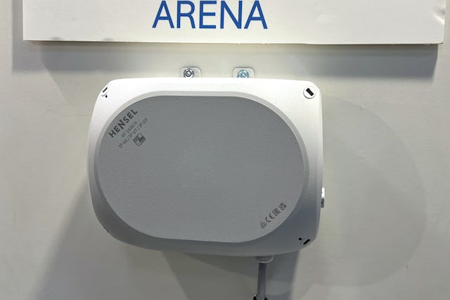 Rektangulär vit Hansel eldosa monterad på väggen under den skrivna skylten "arena"kabeln är ansluten under den.