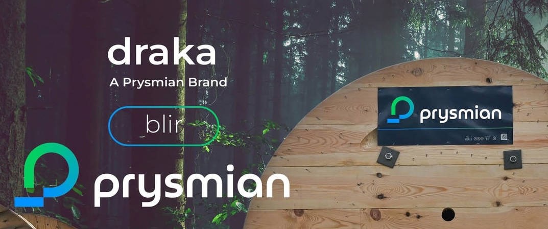 En stor kabeltrumma i trä med Prysmian-loggan och varumärket Draka och Blir sitter framför skogen.