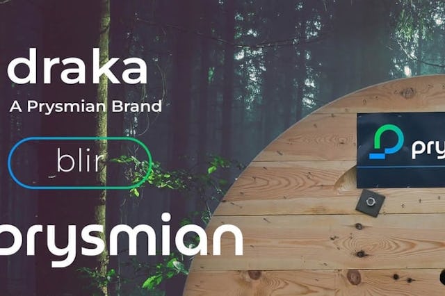 En stor kabeltrumma i trä med Prysmian-loggan och varumärket Draka och Blir sitter framför skogen.