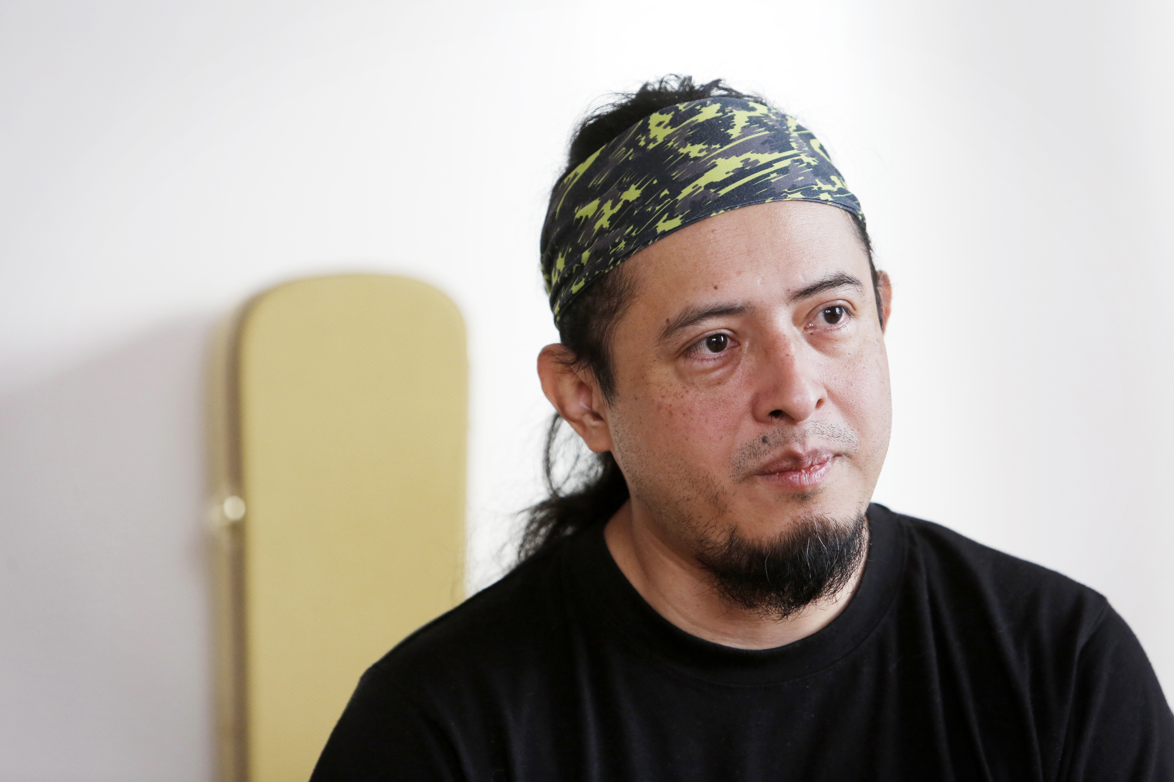 Jonathan, med skägg och mustasch, iklädd mönstrat pannband och svart tröja, sitter inomhus mot en ljus bakgrund.