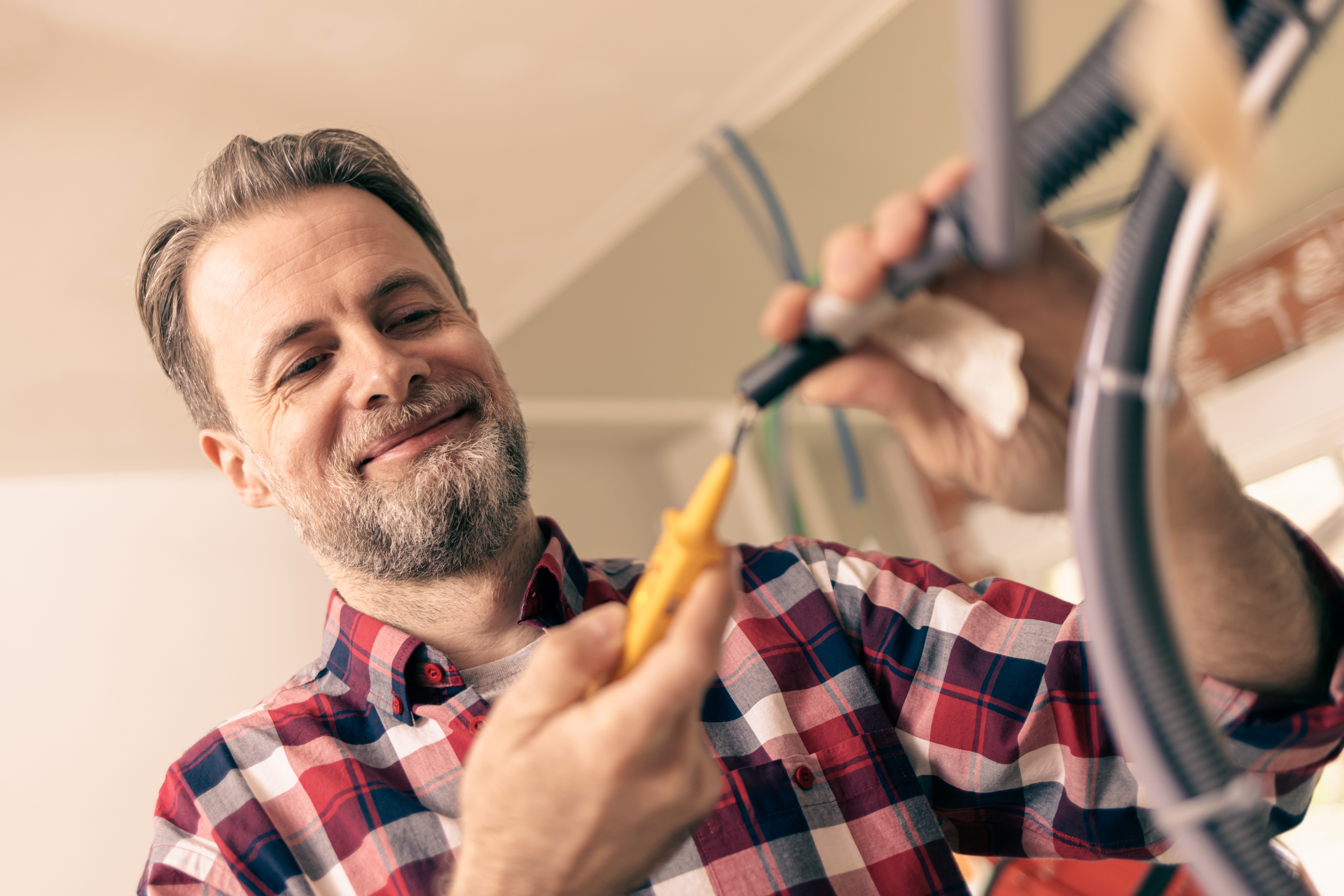 En man som bär en rutig skjorta använder trådskärare för att ta bort isolering från elektriska ledningar inomhus.