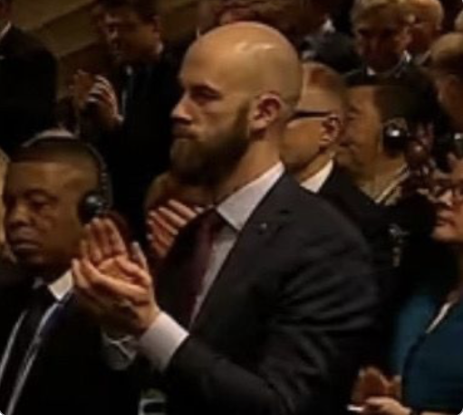 En grupp personer i formella kläder står och applåderar på ett inomhusevenemang; några har hörlurar på sig.