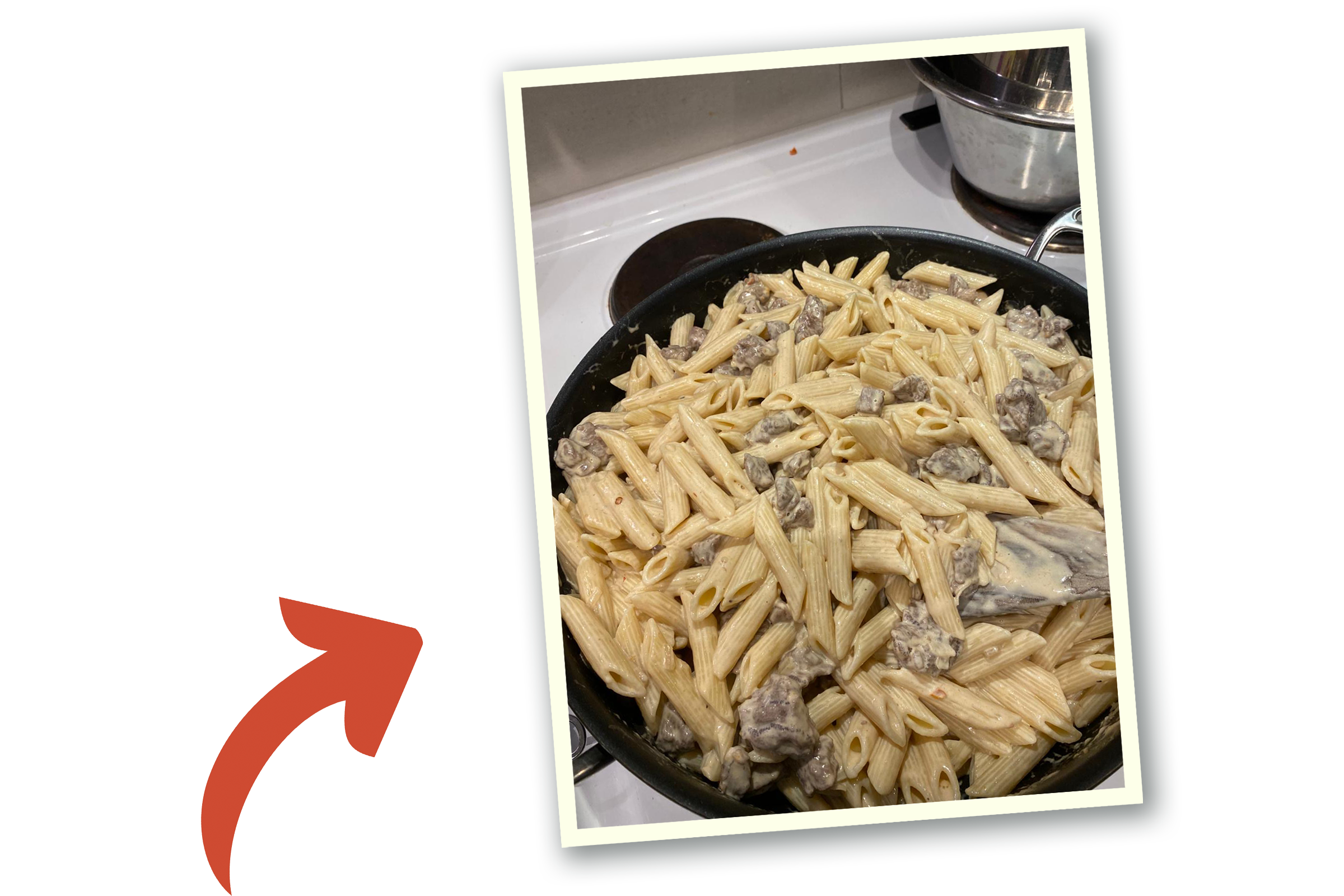 En stekpanna med pasta, sås och biffbitar står på spisen.