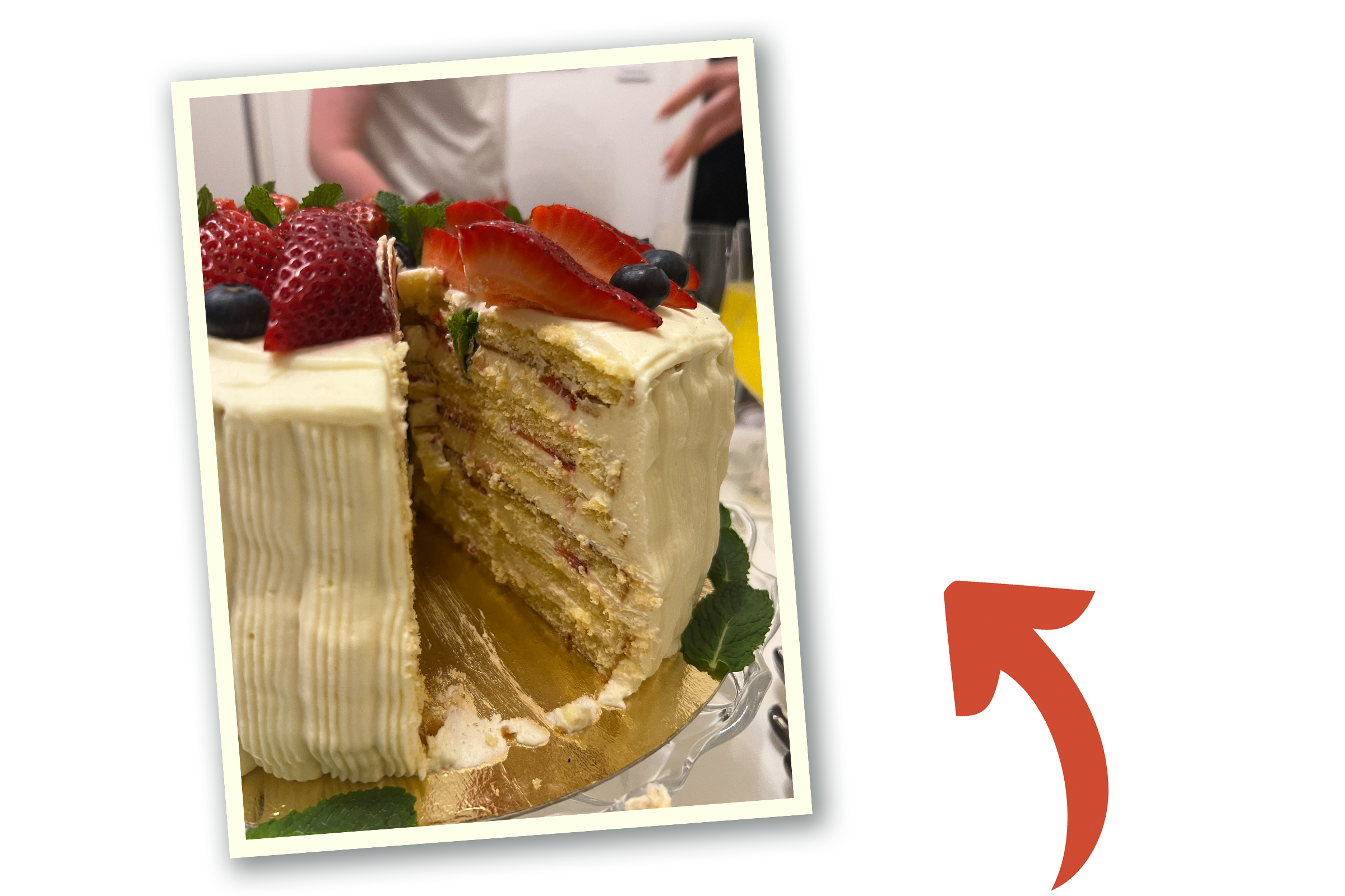 En tårta med vit glasyr och toppad med skivade jordgubbar och blåbär. En röd pil pekar på bilden.