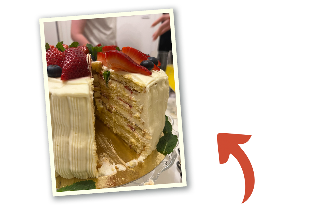 En tårta med vit glasyr och toppad med skivade jordgubbar och blåbär. En röd pil pekar på bilden.