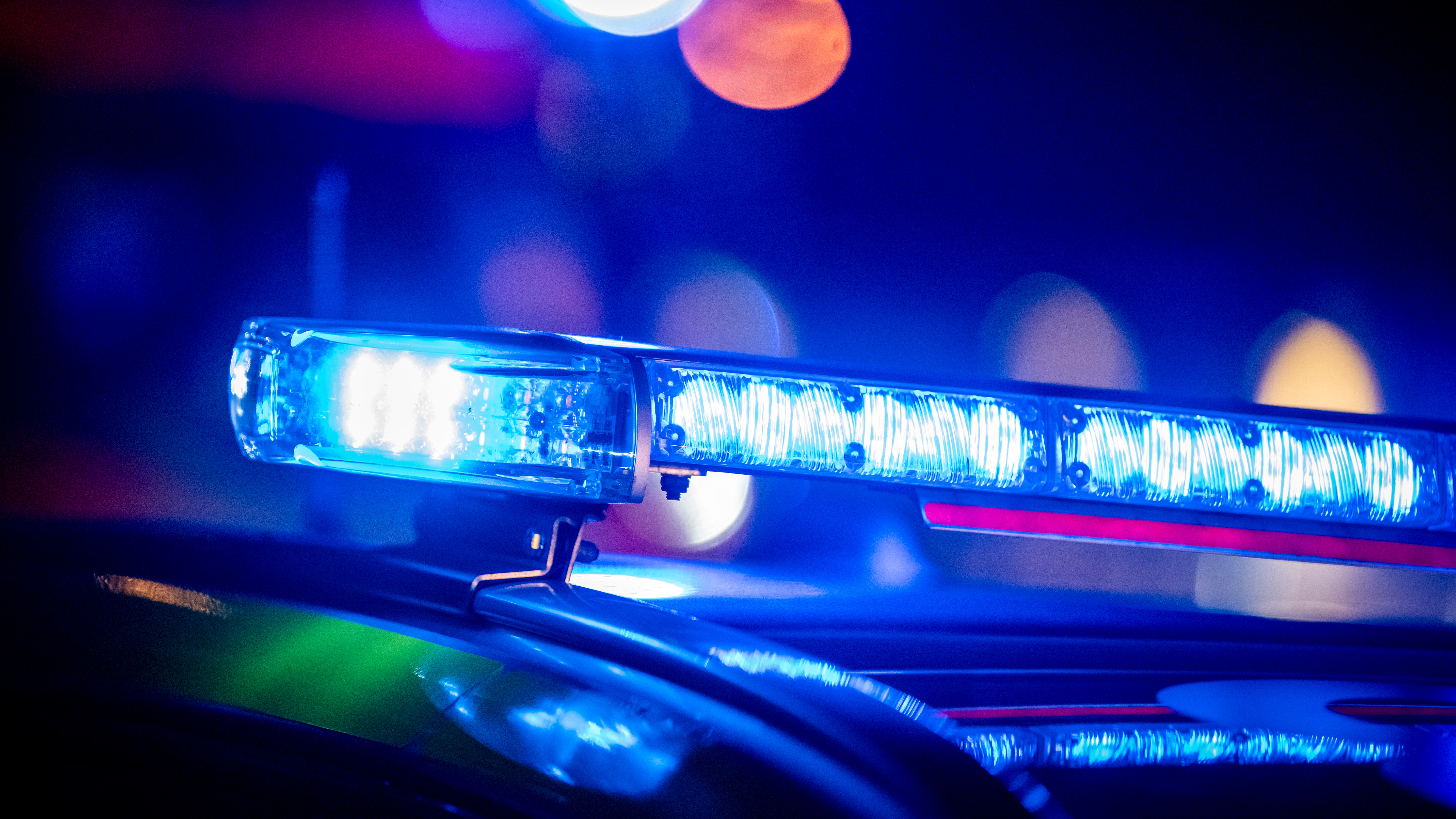 Närbild på ett polisbils tak med blå utryckningsljus som blinkar på natten och otydliga ljus i bakgrunden.