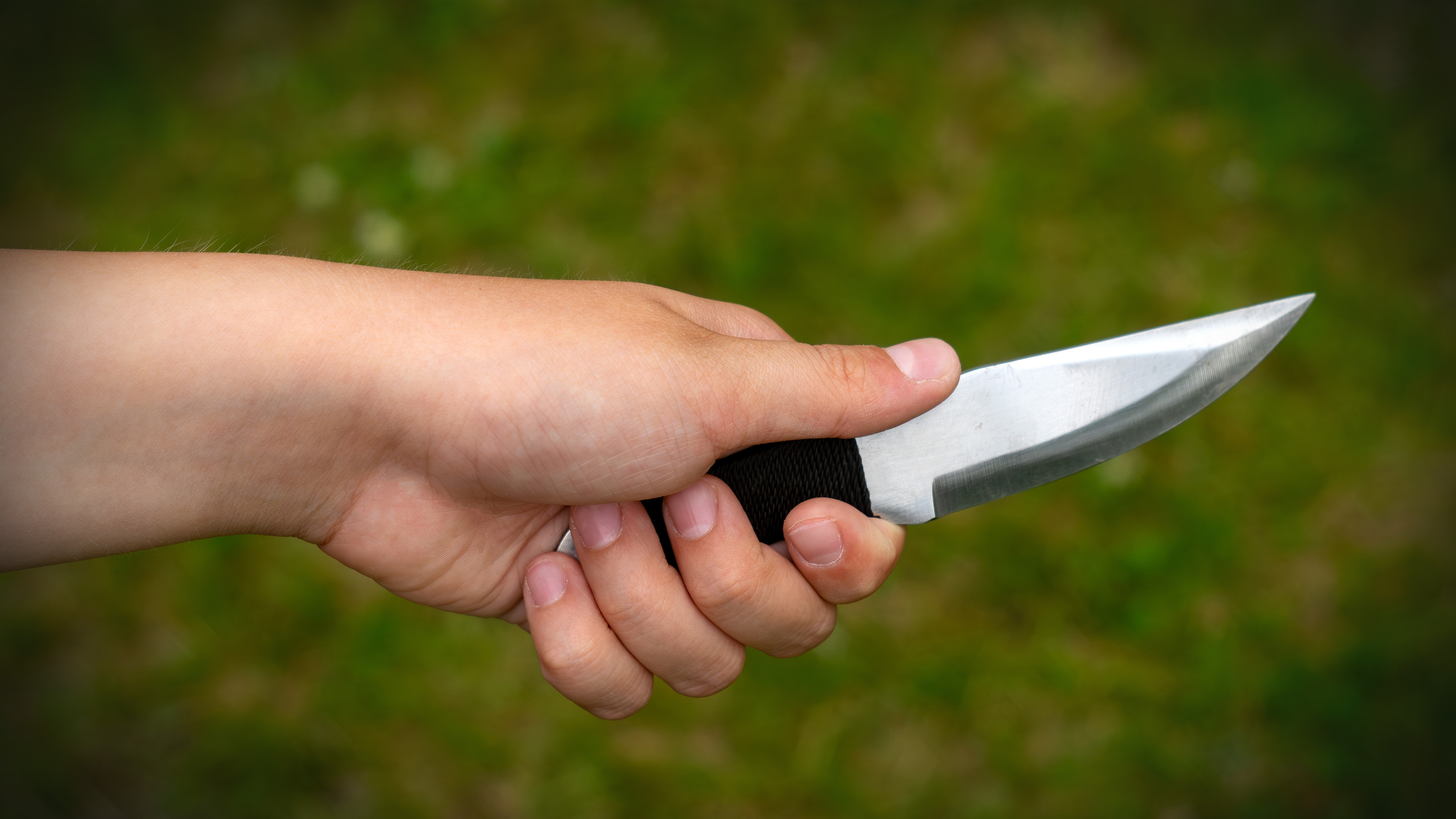 En person håller i en kniv med svart handtag mot en grön, suddig bakgrund.