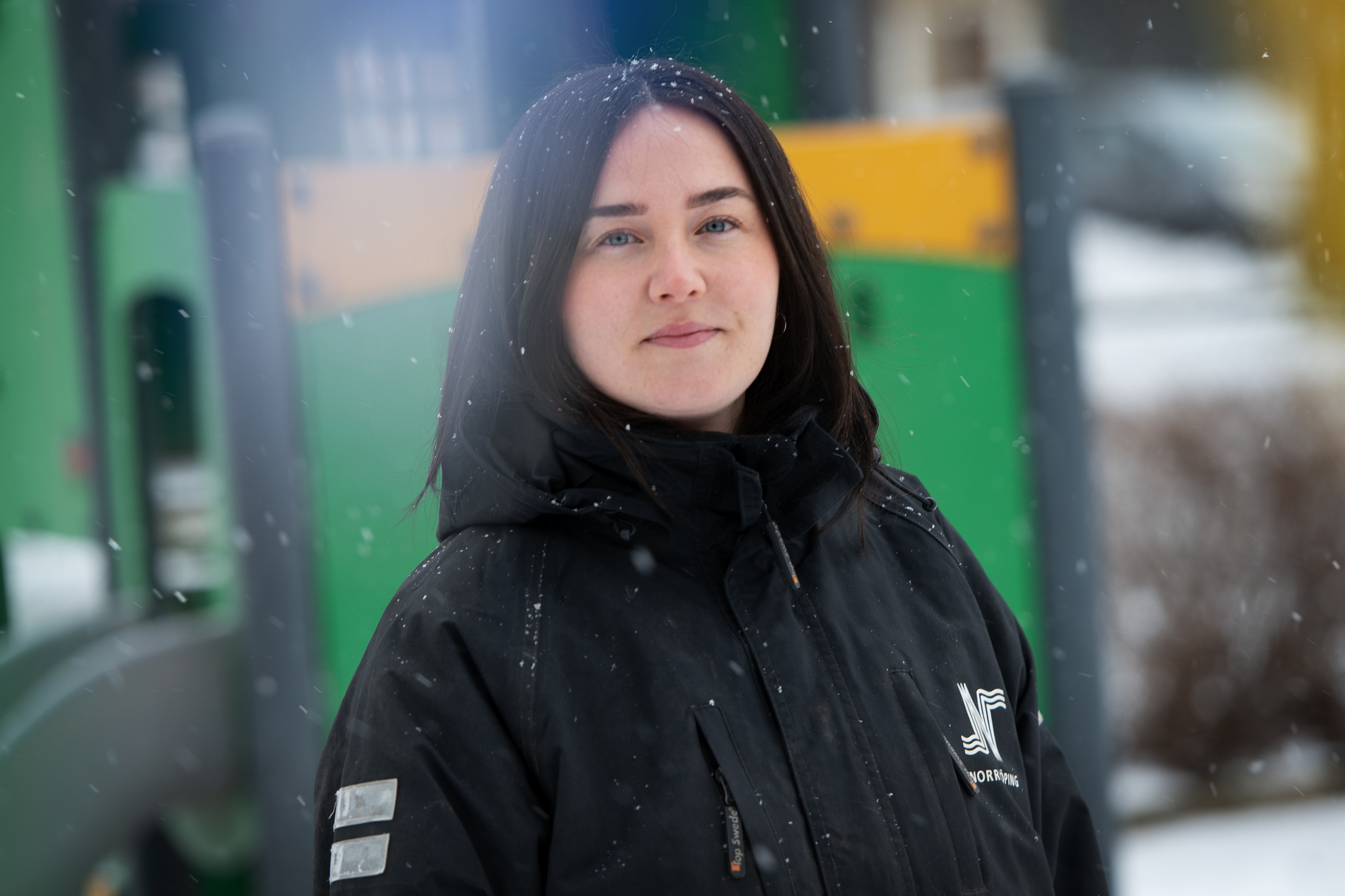 En kvinna i svart vinterjacka står utomhus i snö. I bakgrunden syns gröna och gula lekredskap som är suddiga.