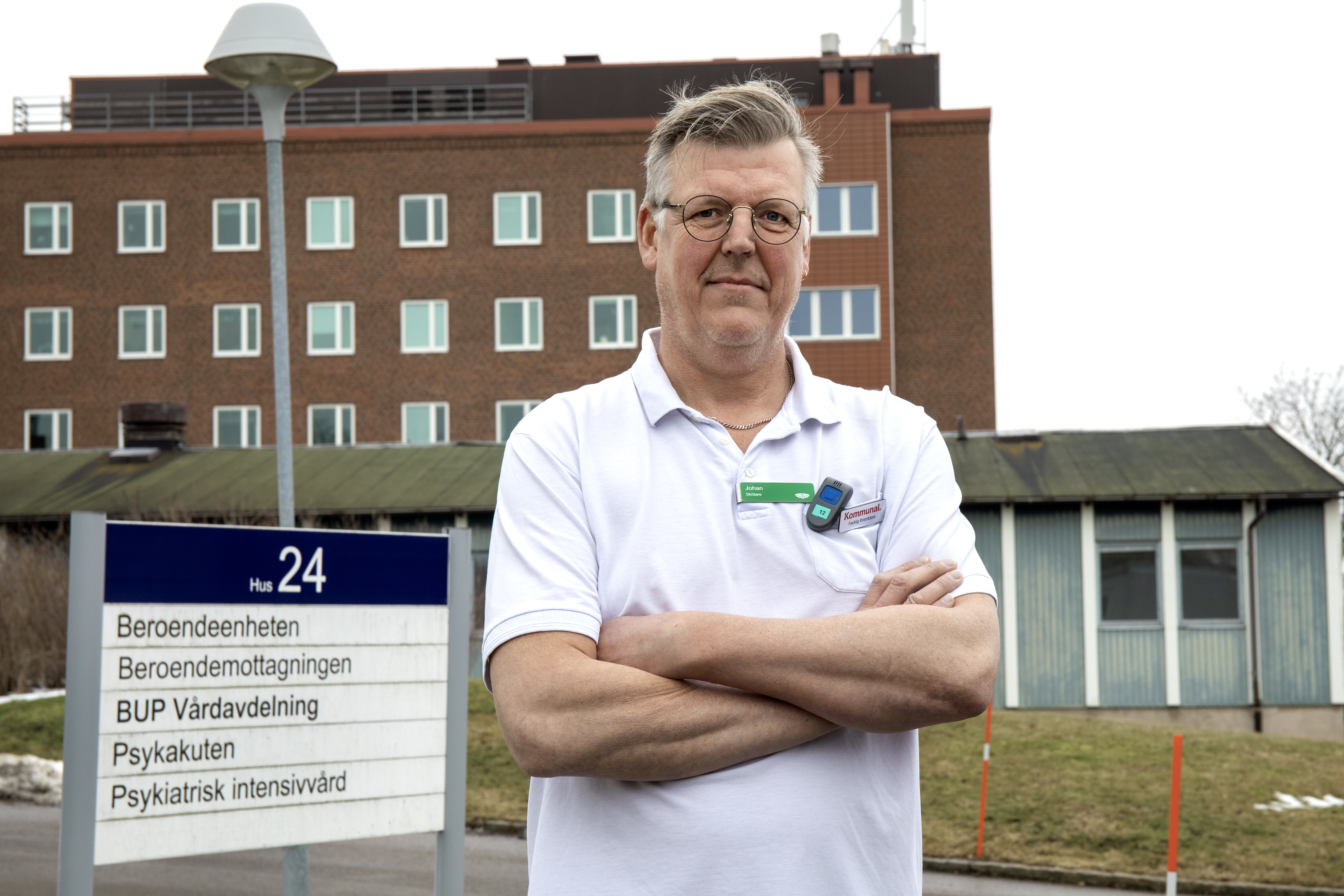 Man i vit pikétröja står utanför en tegelbyggnad.