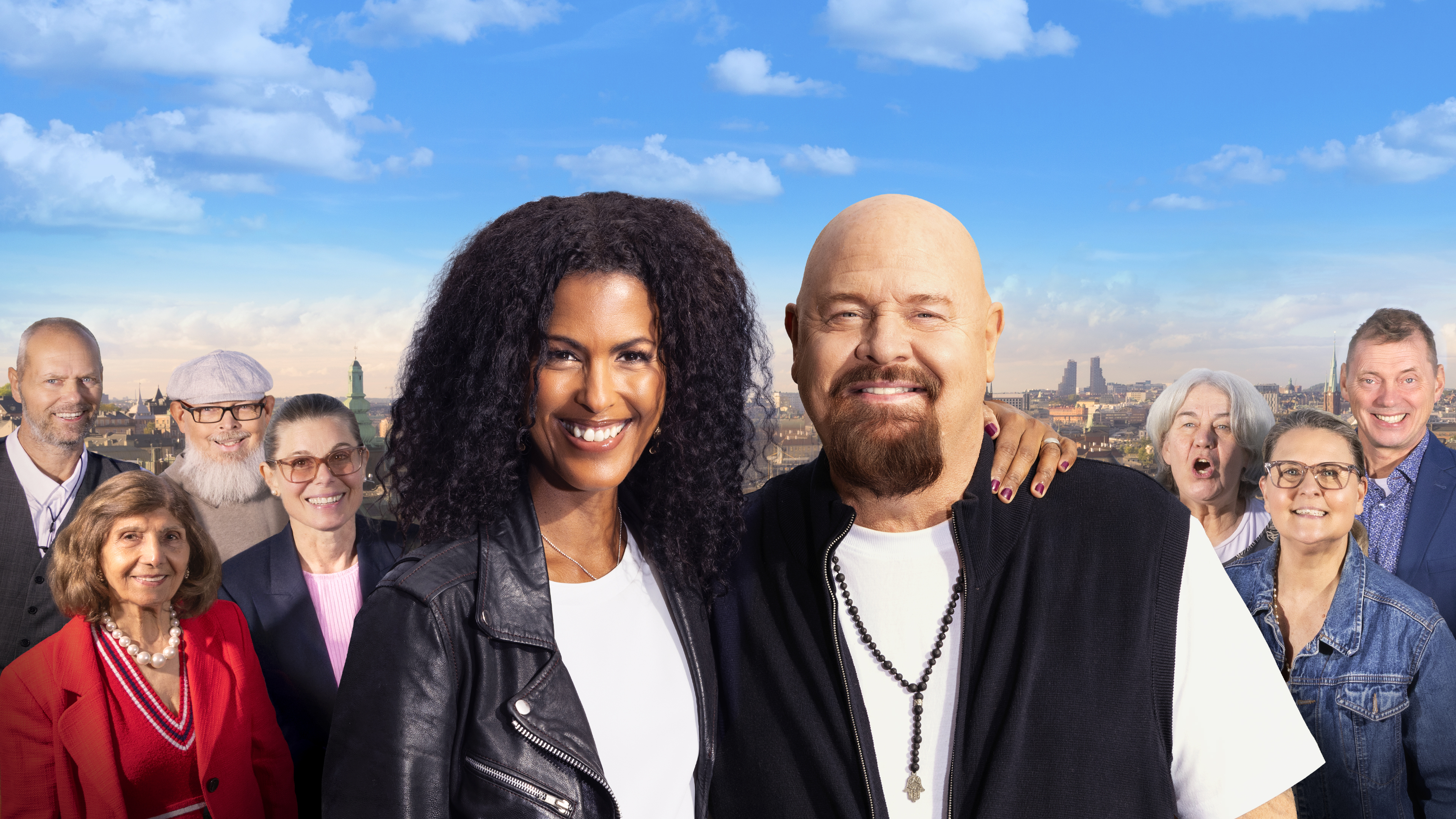 En grupp vuxna står utomhus med en stad och himmel i bakgrunden. Två personer står längst fram, en har armen runt den andra.