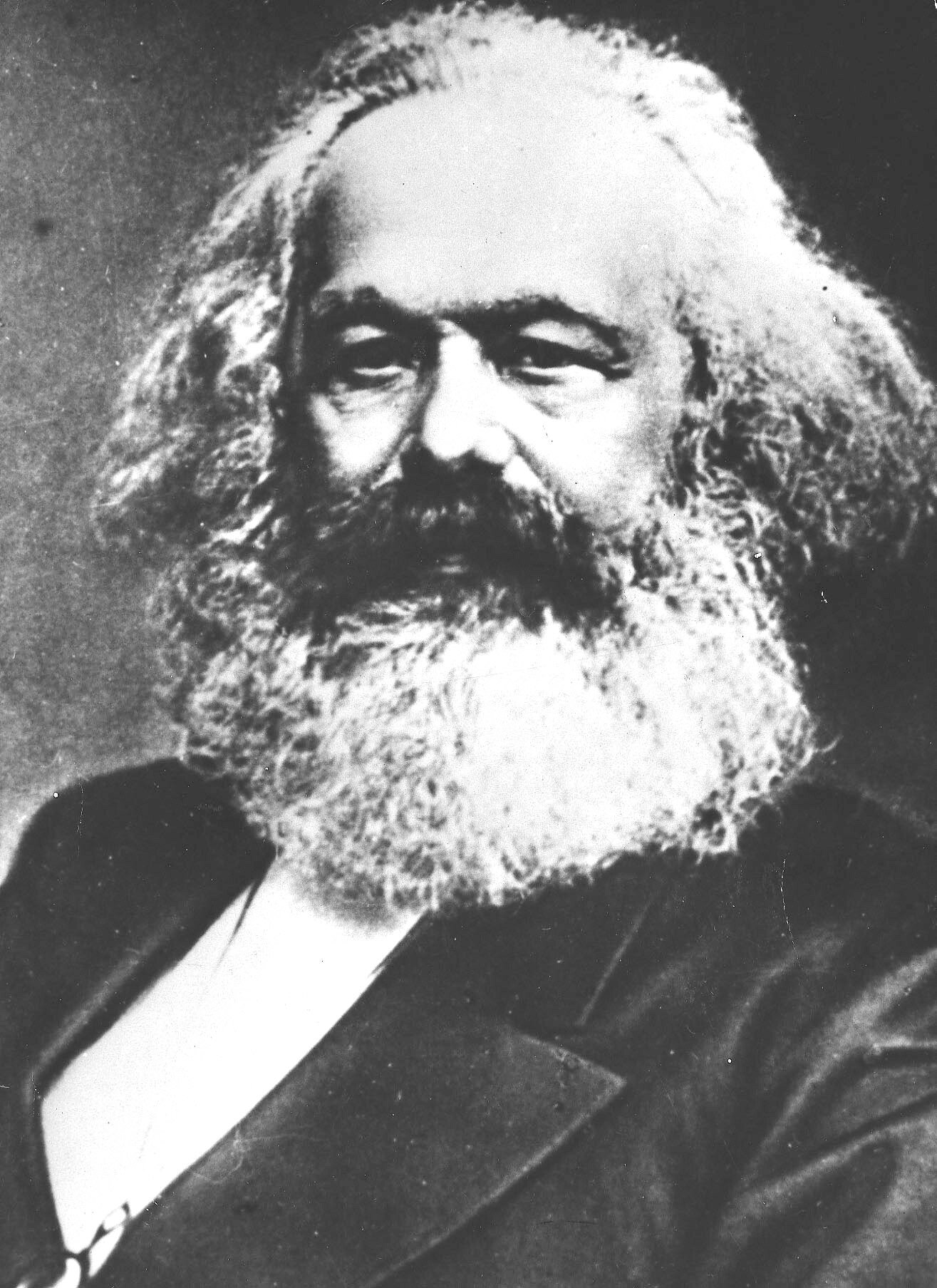 Ett svartvitt porträtt av en äldre man med skägg och mustasch, i mörk kavaj och vit skjorta, som ser mot kameran.
