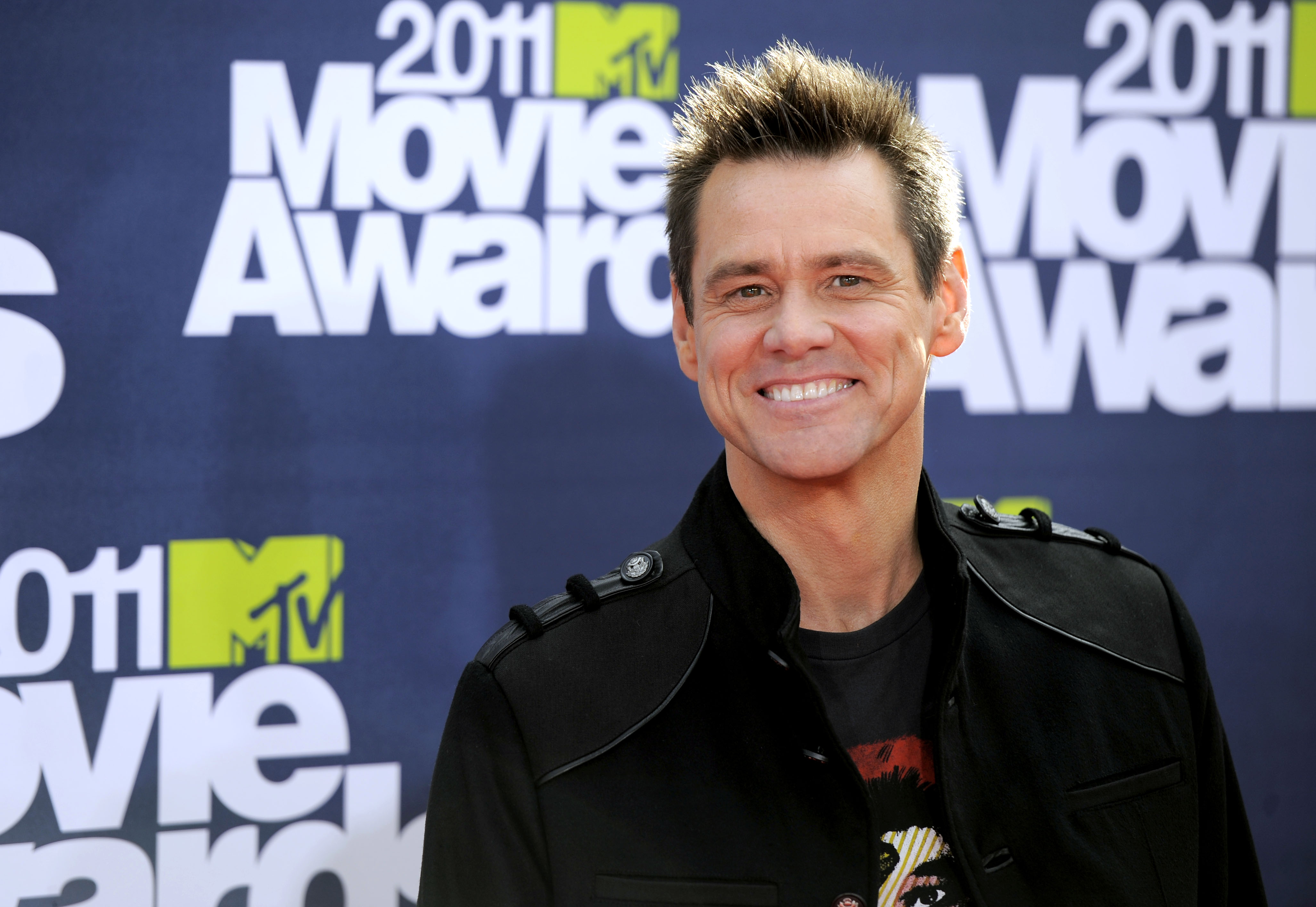 En man i svart jacka ler på röda mattan vid 2011 MTV Movie Awards, med evenemangsskyltar i bakgrunden.