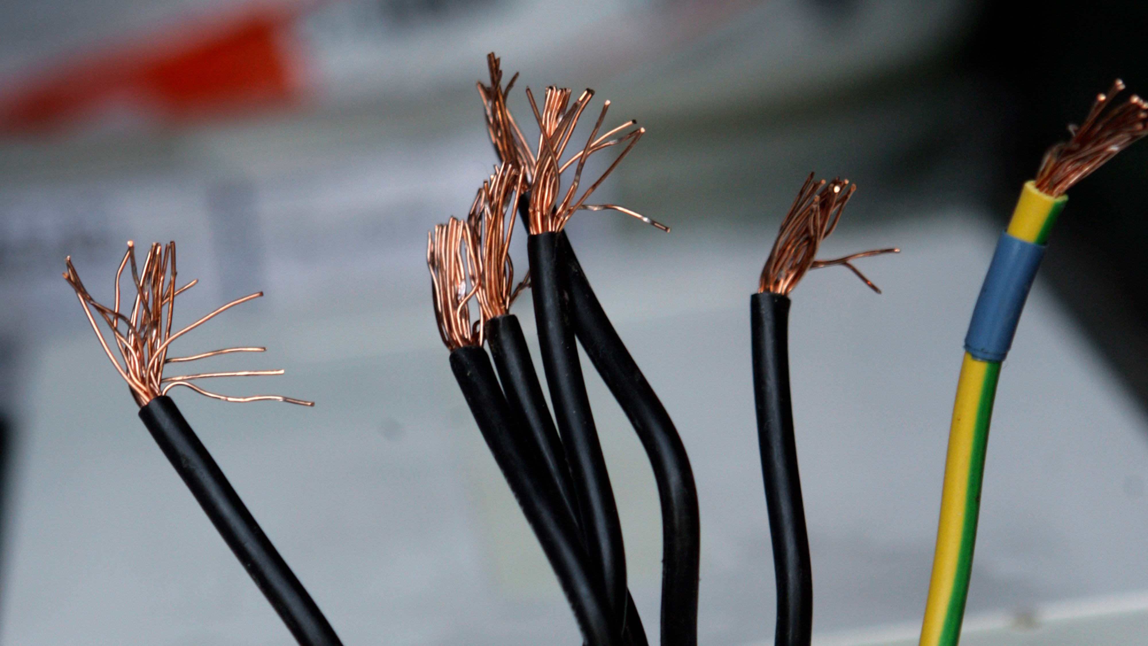 Flera svarta elkablar med synliga koppartrådar och en grön-gulrandig kabel visas mot en suddig bakgrund.