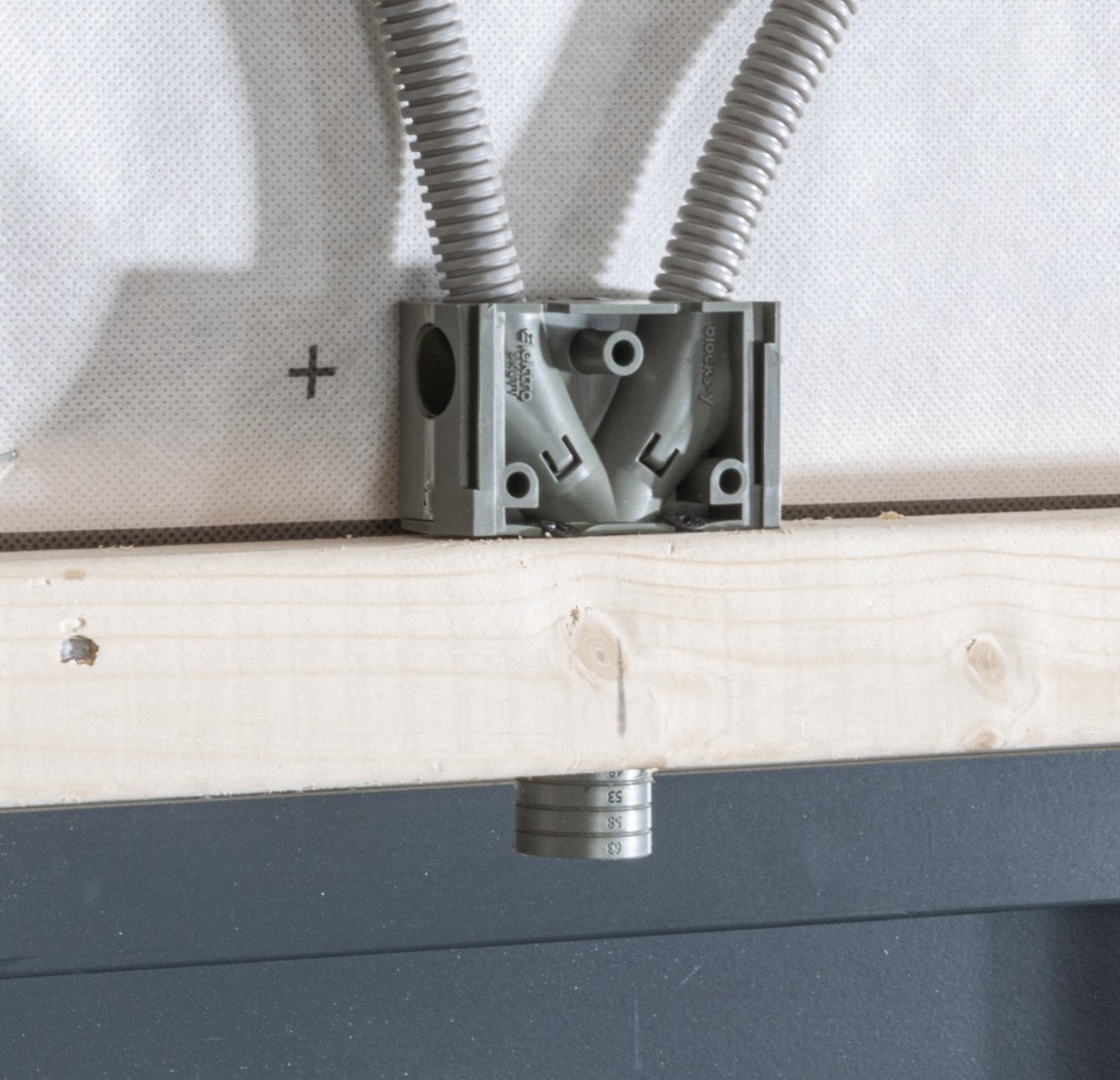 En elektrisk kopplingsdosa med två flexibla rör är monterad på en träskiva, med ett cylindriskt metallföremål under.