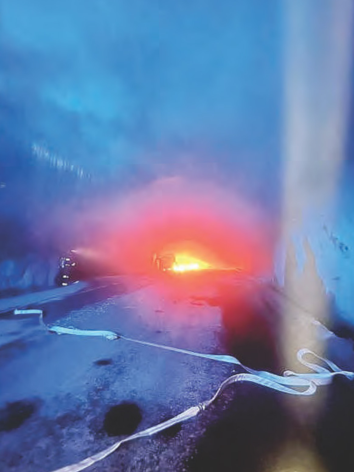 En brand pågår i en tunnel, röken sprider sig och brandslangar ligger utlagda på det våta tunnelgolvet.