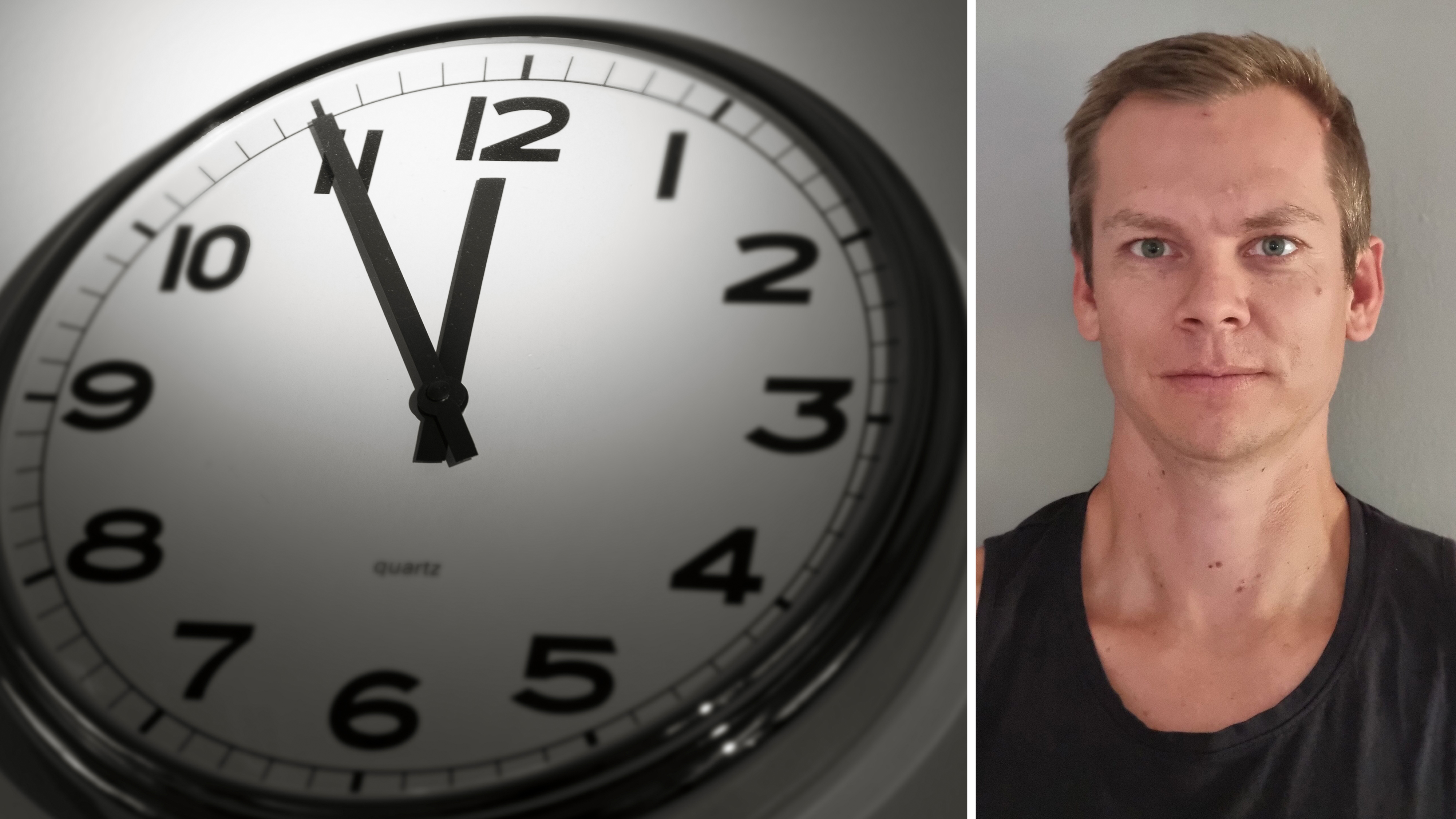 En rund väggklocka som visar 12:01 är till vänster; till höger står en man med kort hår i ärmlös tröja, ser mot kameran.