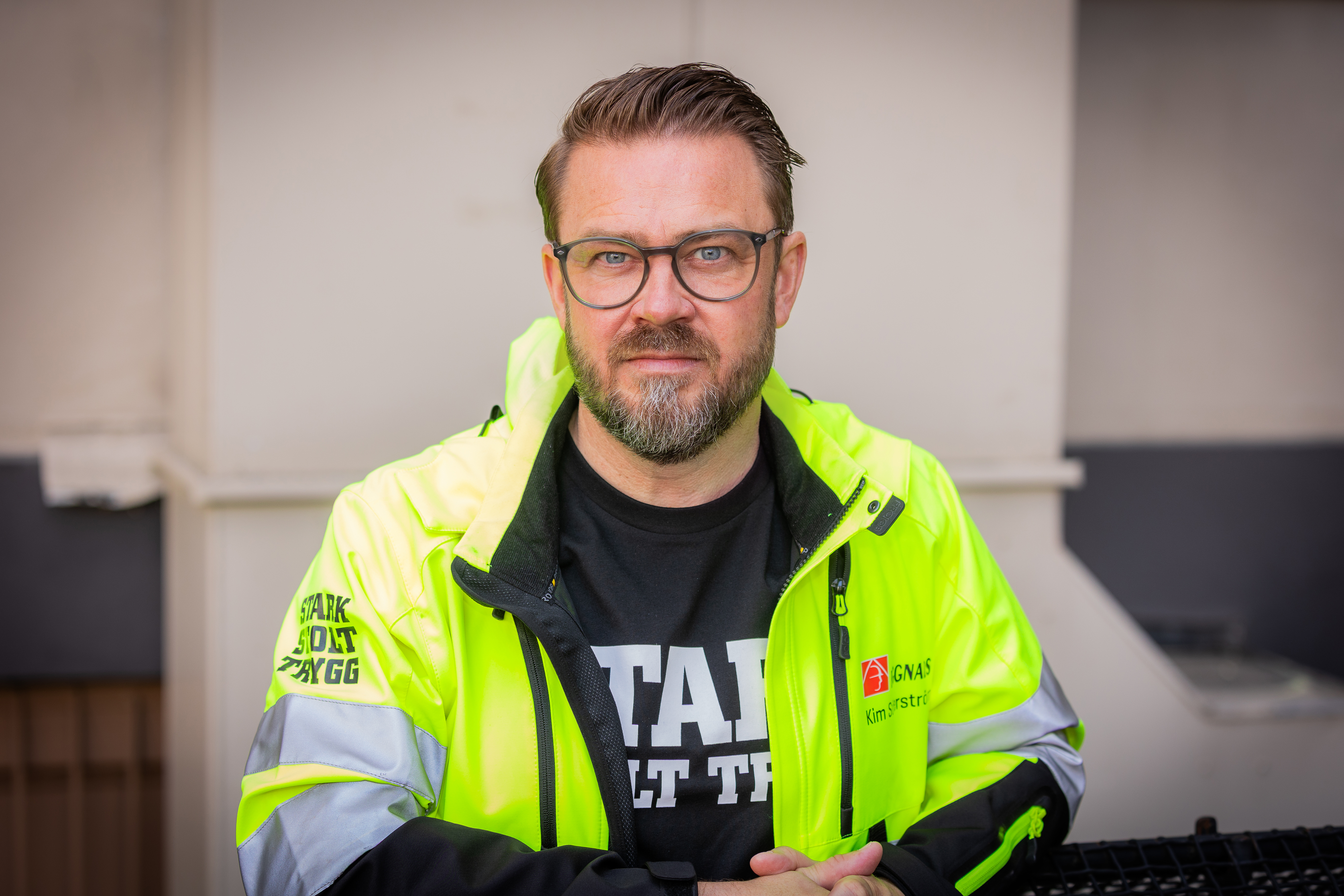 Kim Söderström med glasögon och skägg har på sig en gul jacka och en svart t-shirt, står inomhus mot en neutral bakgrund.