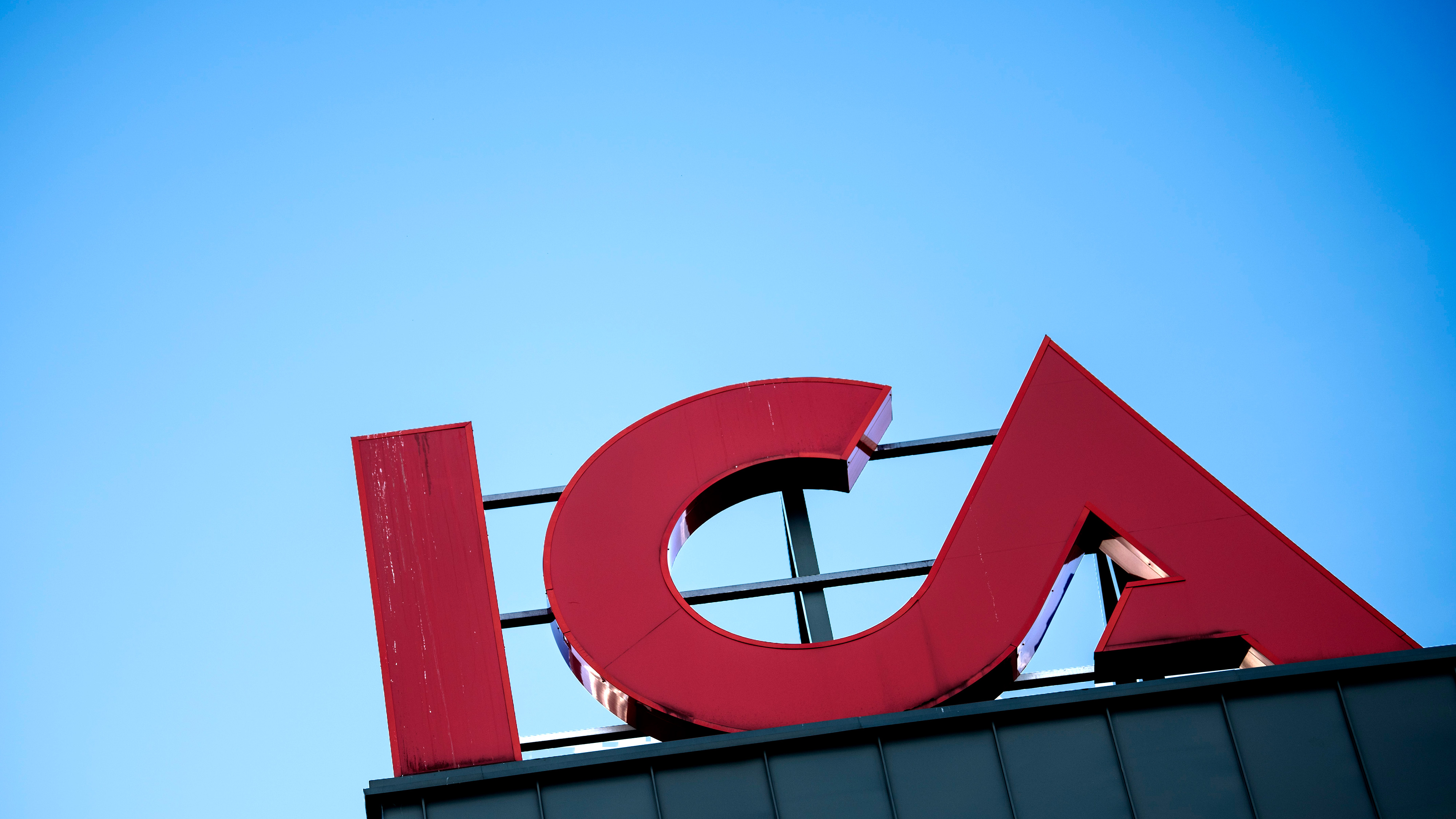 Stora röda bokstäver som bildar ordet "ICA" sitter på en byggnad med en blå himmel i bakgrunden.
