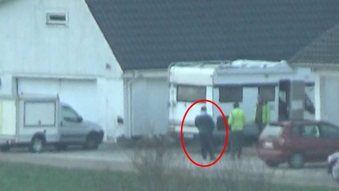 Tre personer står nära en vit husbil och ett garage. En person i mitten är markerad med röd cirkel.