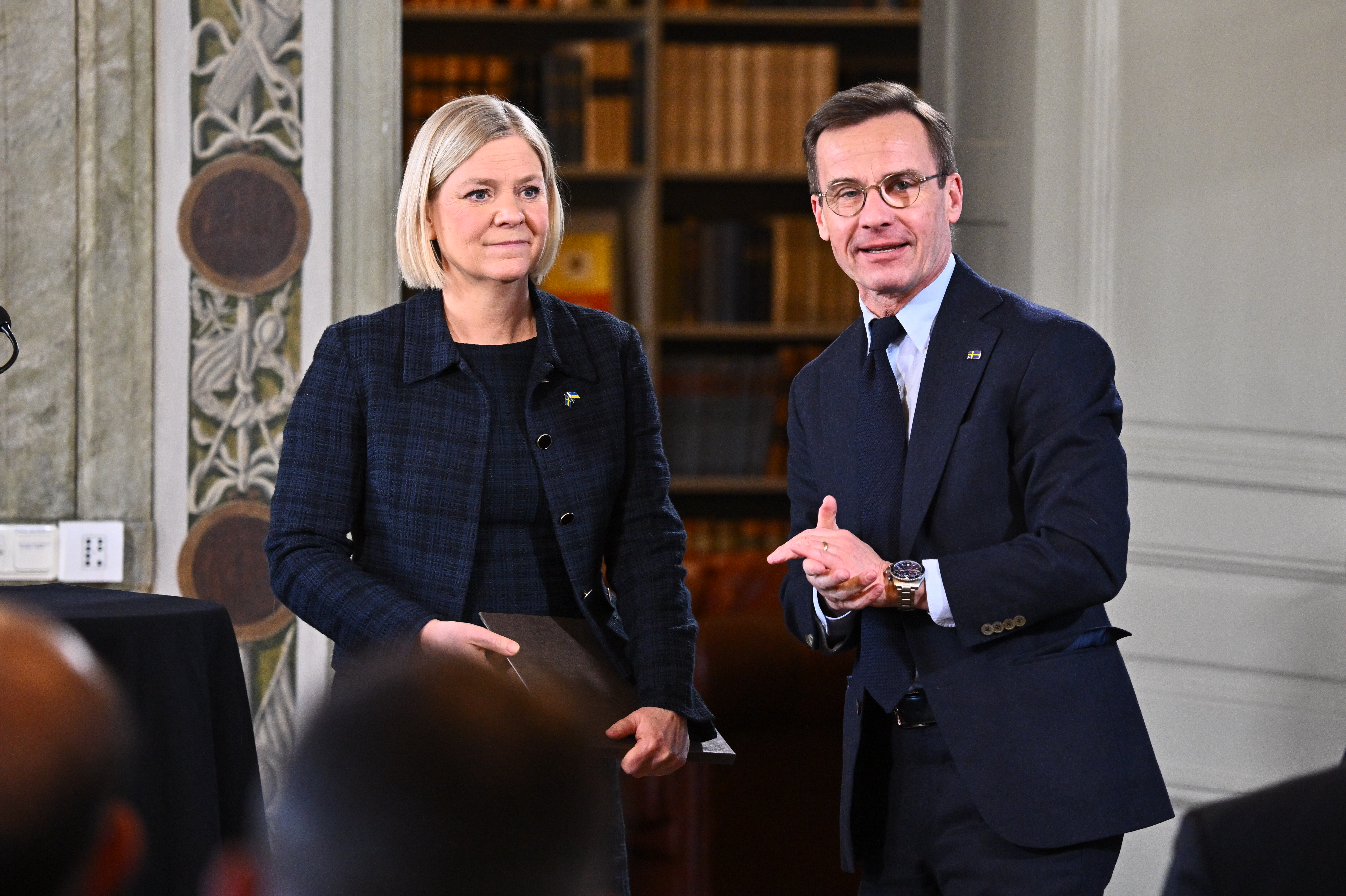 En kvinna i blont hår och en man med glasögon står bredvid varandra.