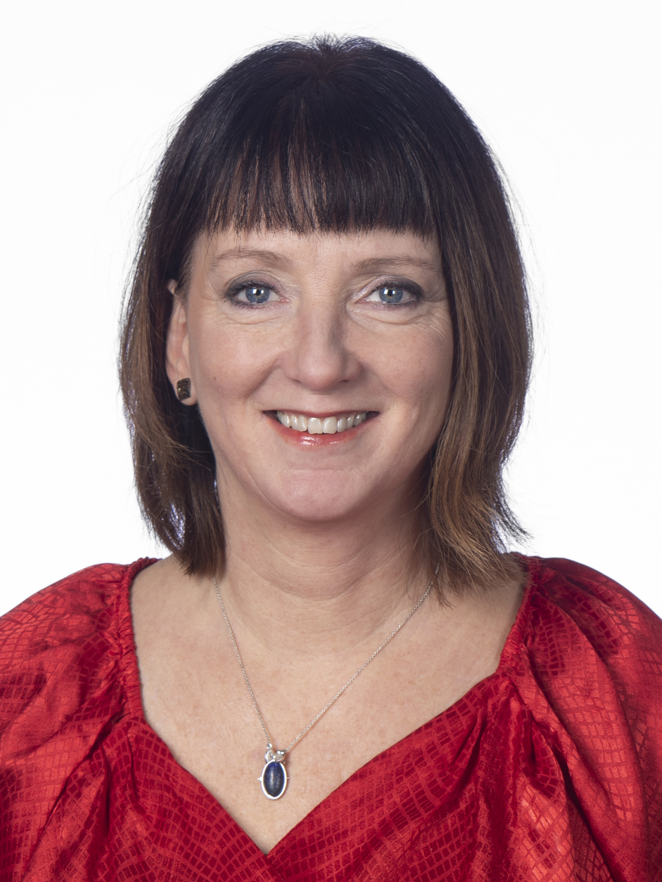 Marina Johansson med brunt axellångt hår och lugg har på sig en röd topp och ett silverhalsband med mörkt hänge, framför vit bakgrund.