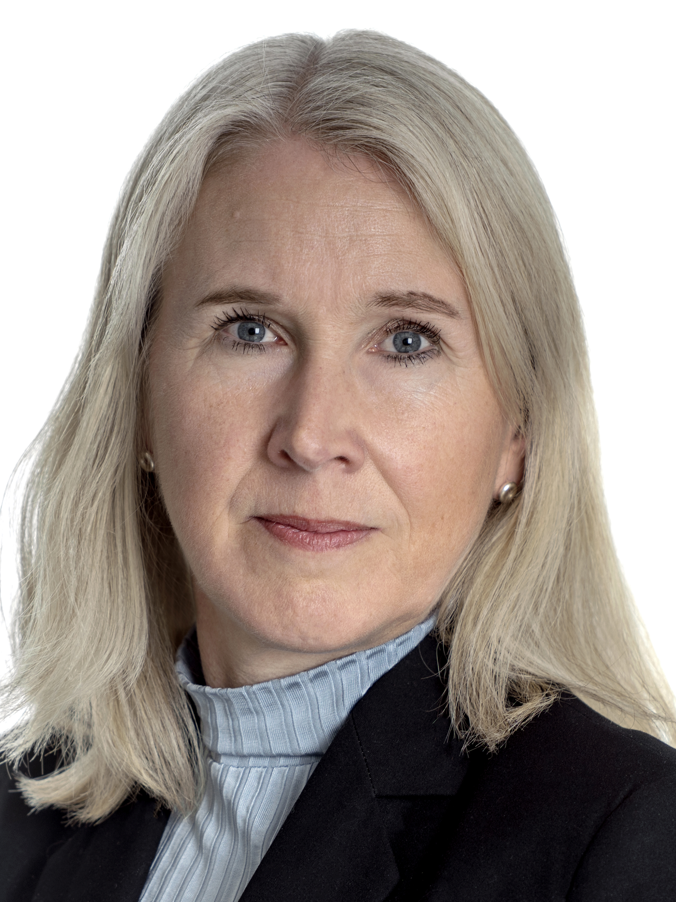 Tina Isaksson med rakt, axellångt grått hår, i ljusblå blus med hög krage och svart kavaj, ser in i kameran mot vit bakgrund.