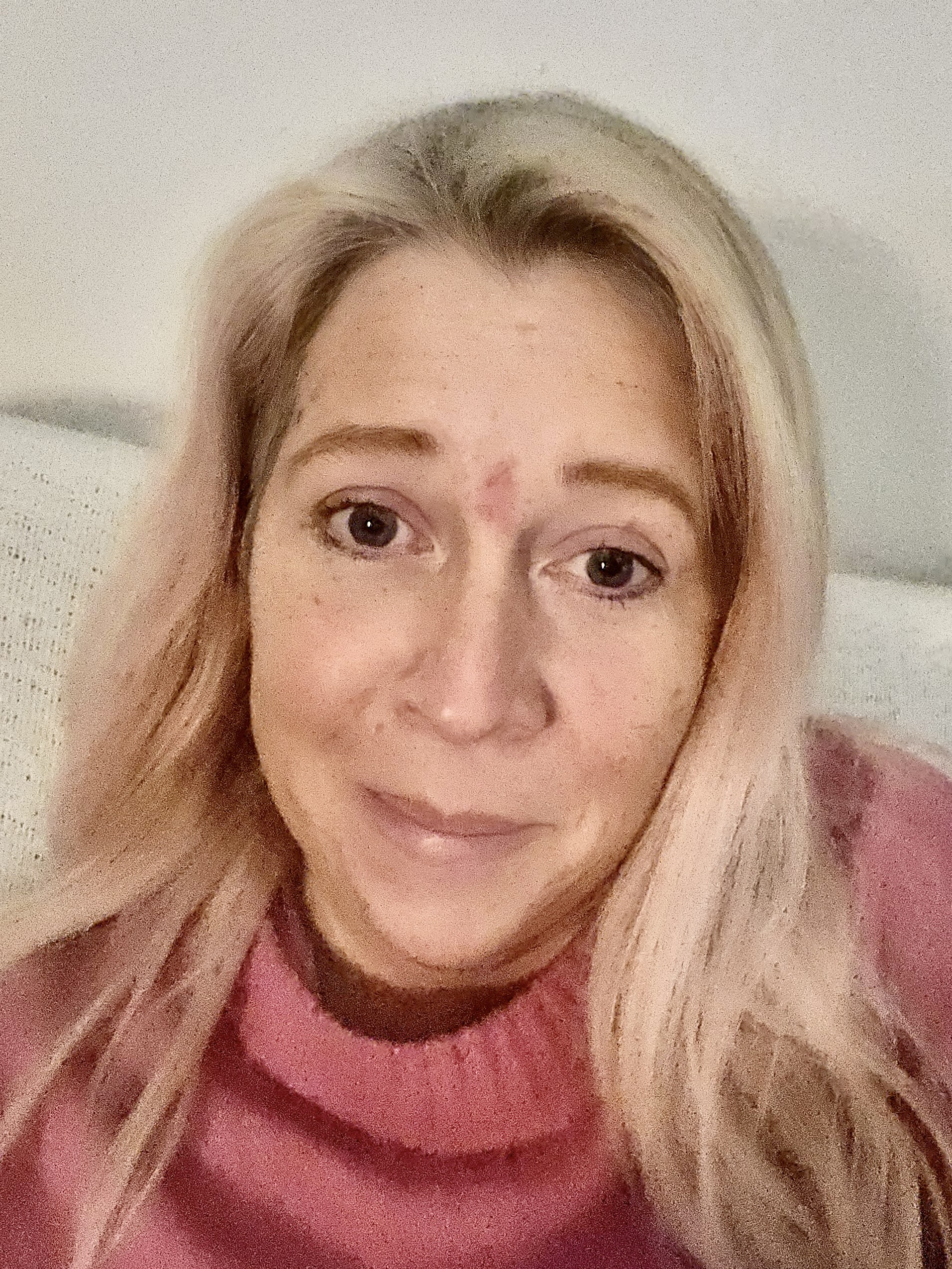 Lisa Sjölin med långt blont hår och en rosa tröja sitter inomhus och tittar mot kameran med ett svagt leende.