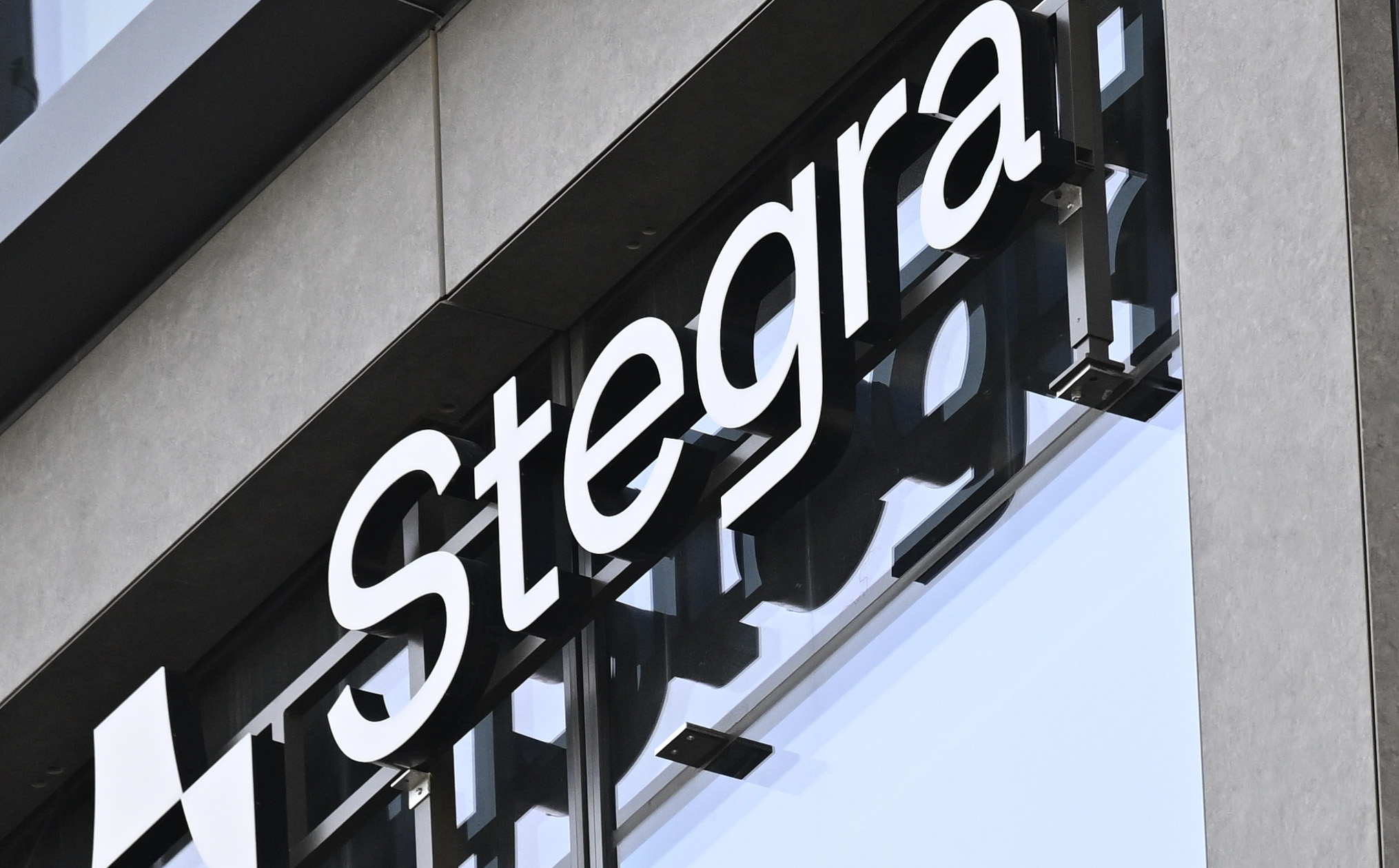 En byggnadsfasad med stora fönster visar ordet "Stegra" i vita bokstäver på en svart skylt.
