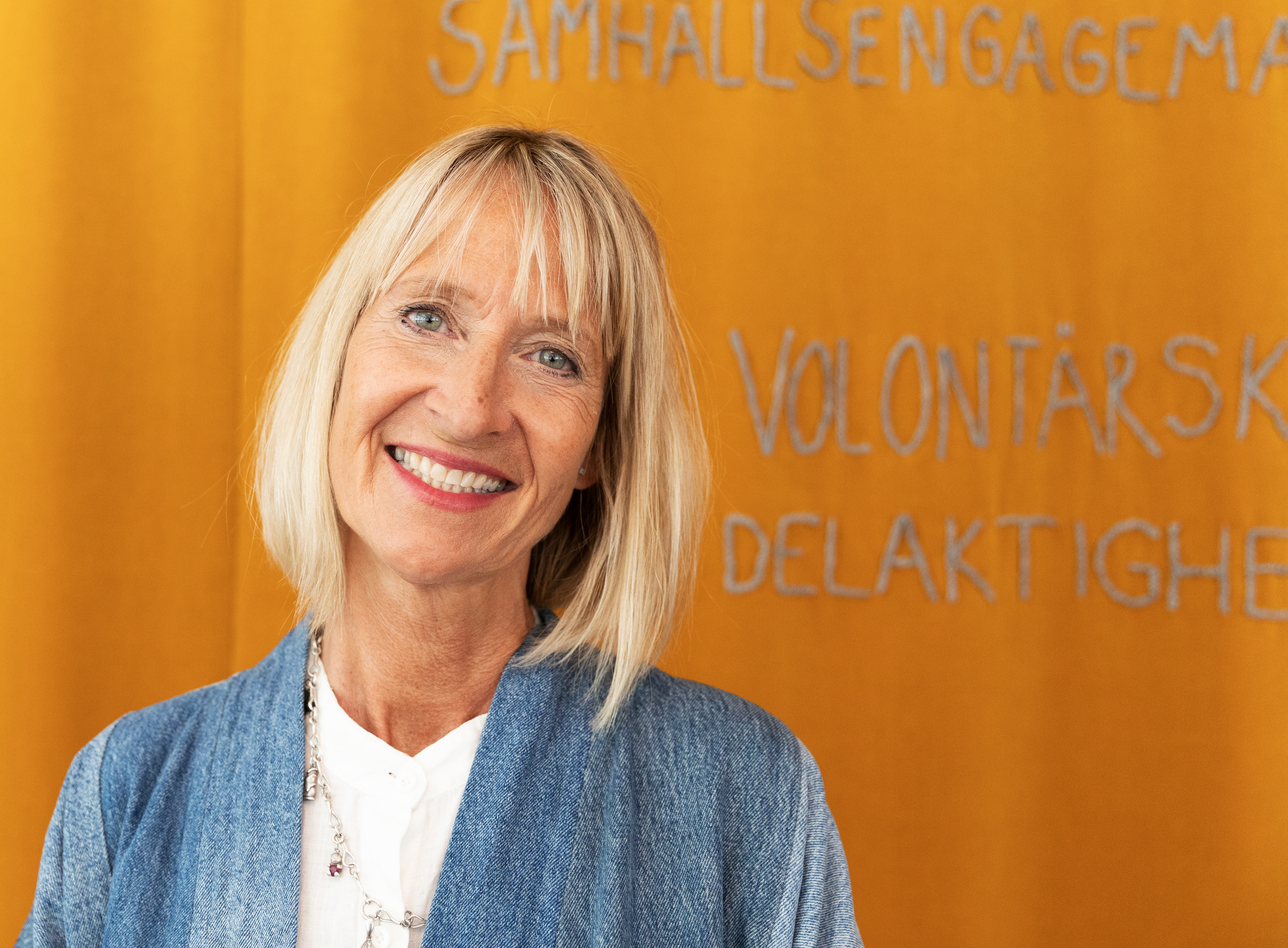Åsa Paborn med blont hår står framför en gul bakgrund med svensk text.