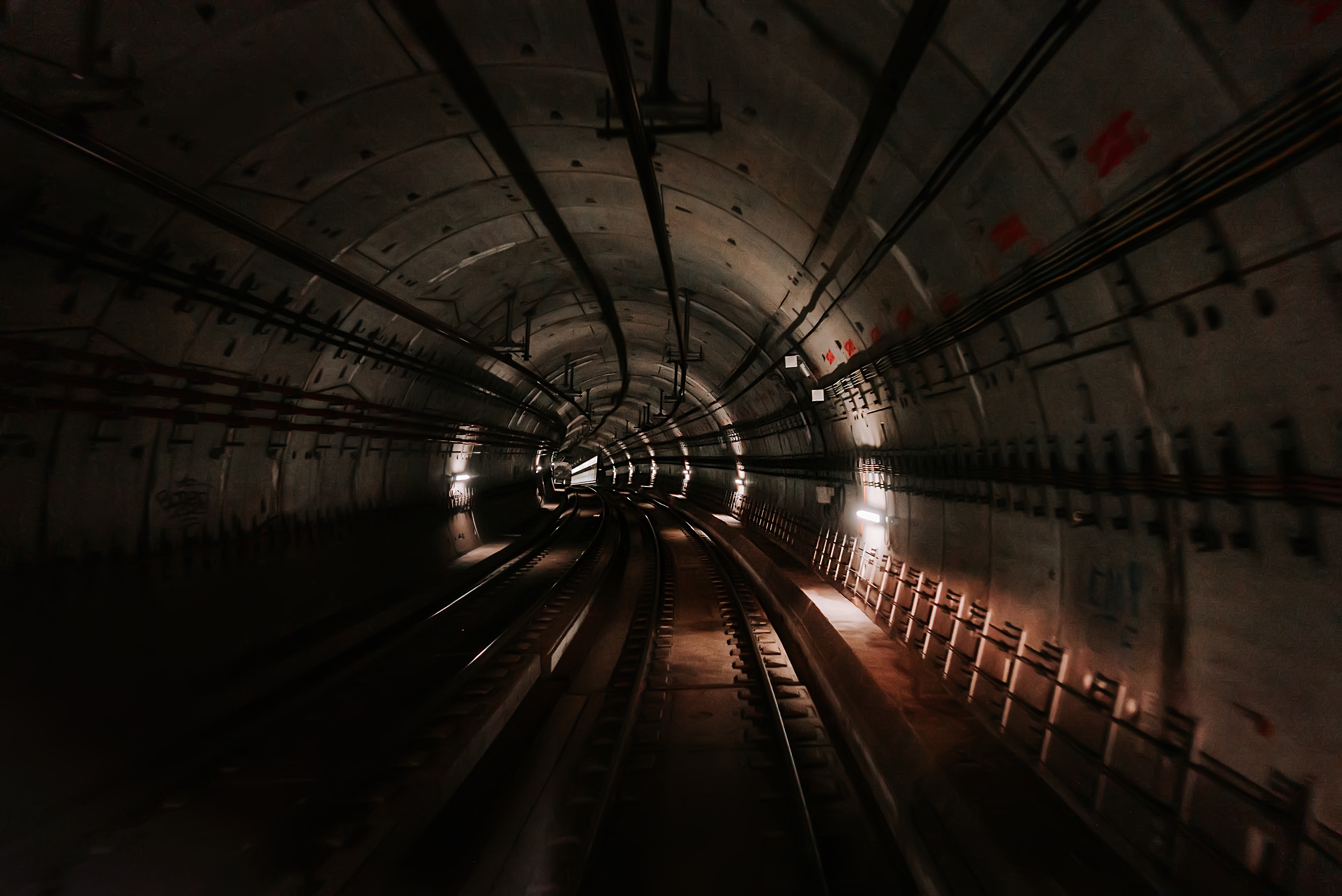 En tunnelbana med flera svajande spår. Den är upplyst av lampor placerade med mellanrum på väggen.