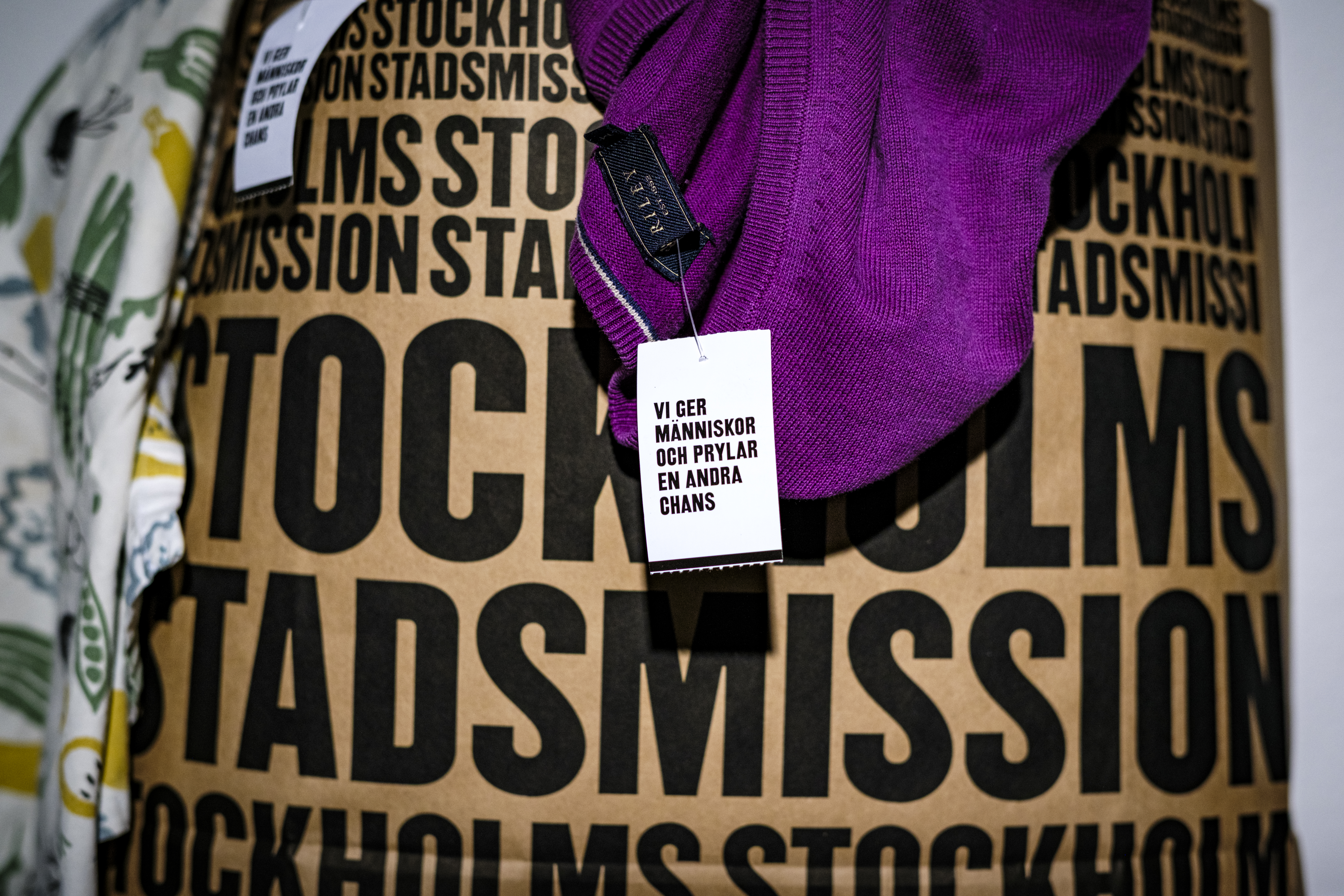 En påse med texten "STOCKHOLMS STADSMISSION" tryckt i svart, ett plagg ovanpå samt en lapp med texten ”Vi ger människor och prylar en andra chans”.