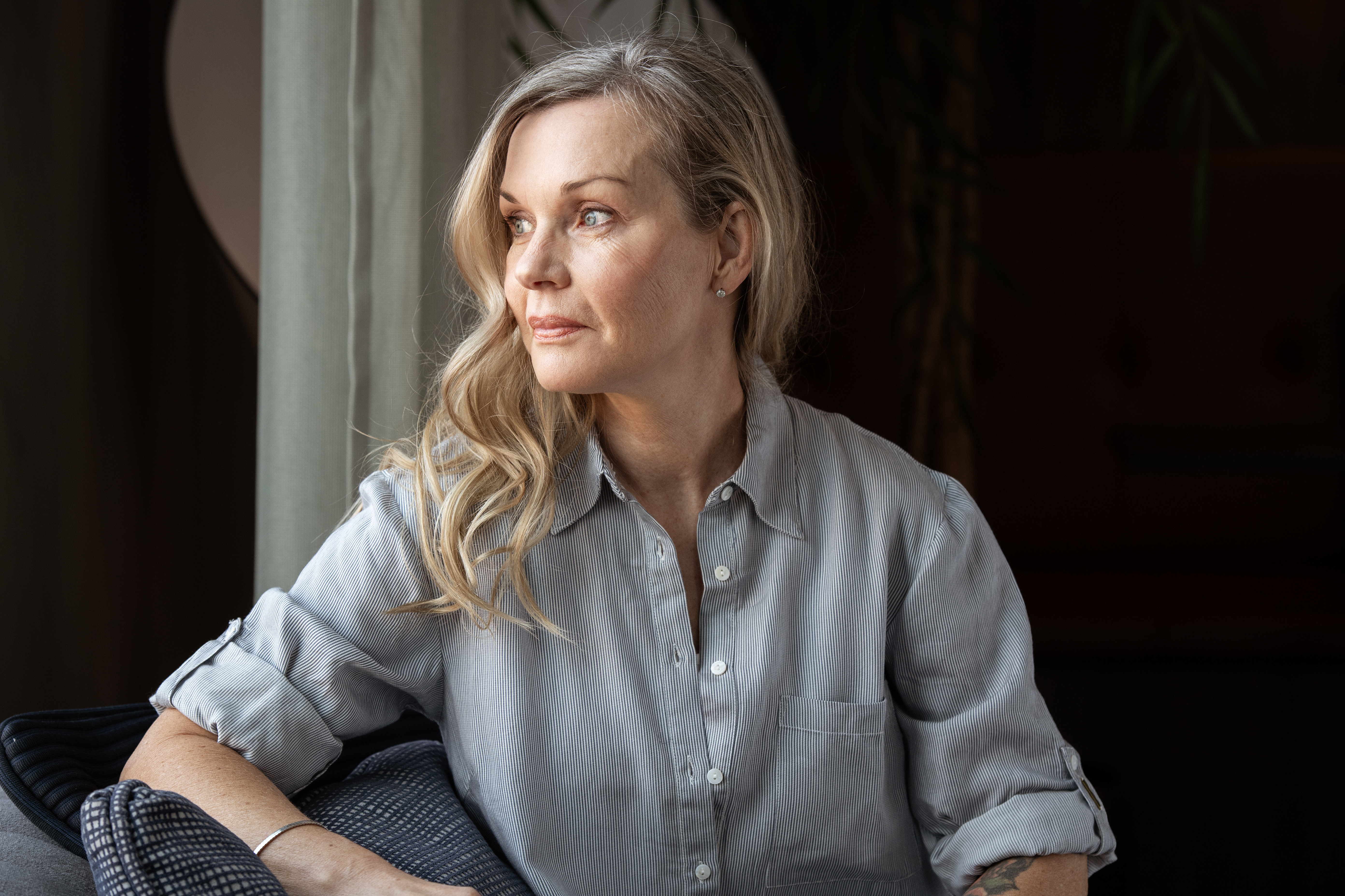 Pia Johansson med långt blont hår och en ljusgrå skjorta sitter inomhus och ser åt höger, utanför bild.