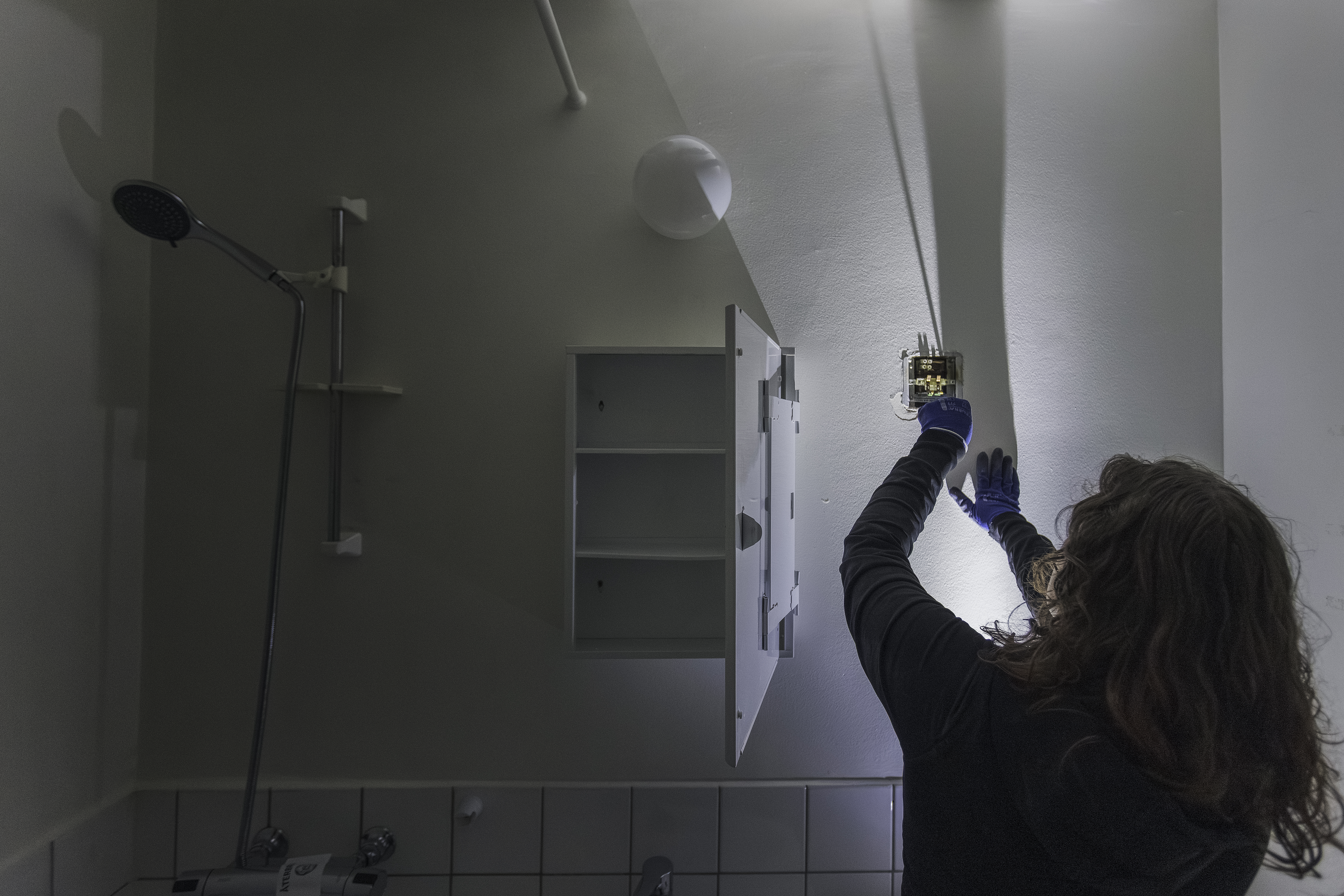 I närheten kan man se en handskar som sätter in skruvar i ett badrums eluttag, ett duschhuvud och ett öppet skåp.