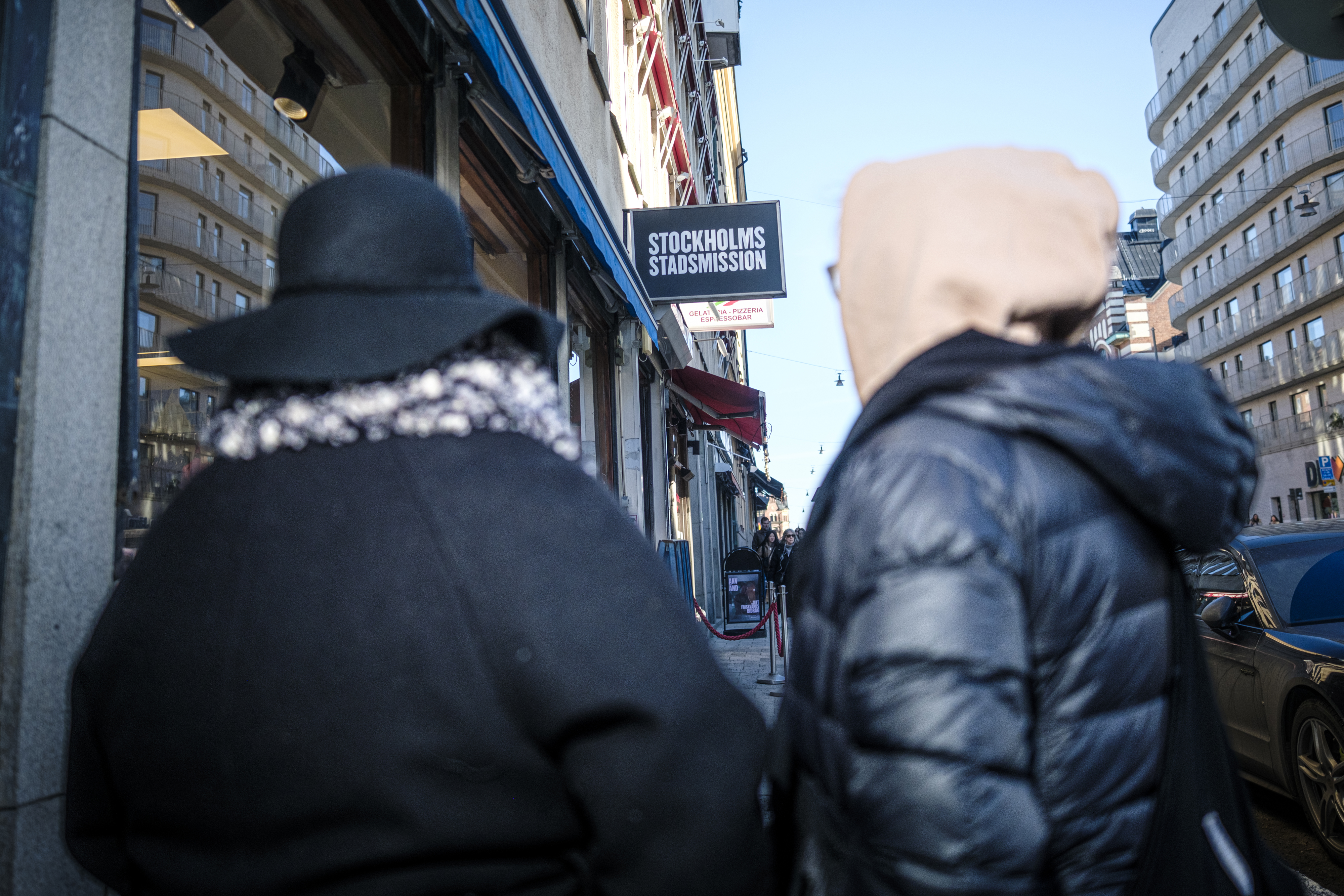 Två personer i jackor står på en stadsgata bredvid en byggnad med en skylt med texten ``Stockholms Stadshus''.