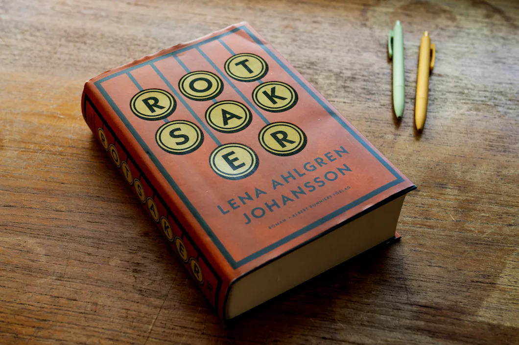 inbunden bok, "rötter" Detta verk av Lena Ahlgren Johansson sitter på ett bord bredvid två pennor, en gul och en grön.
