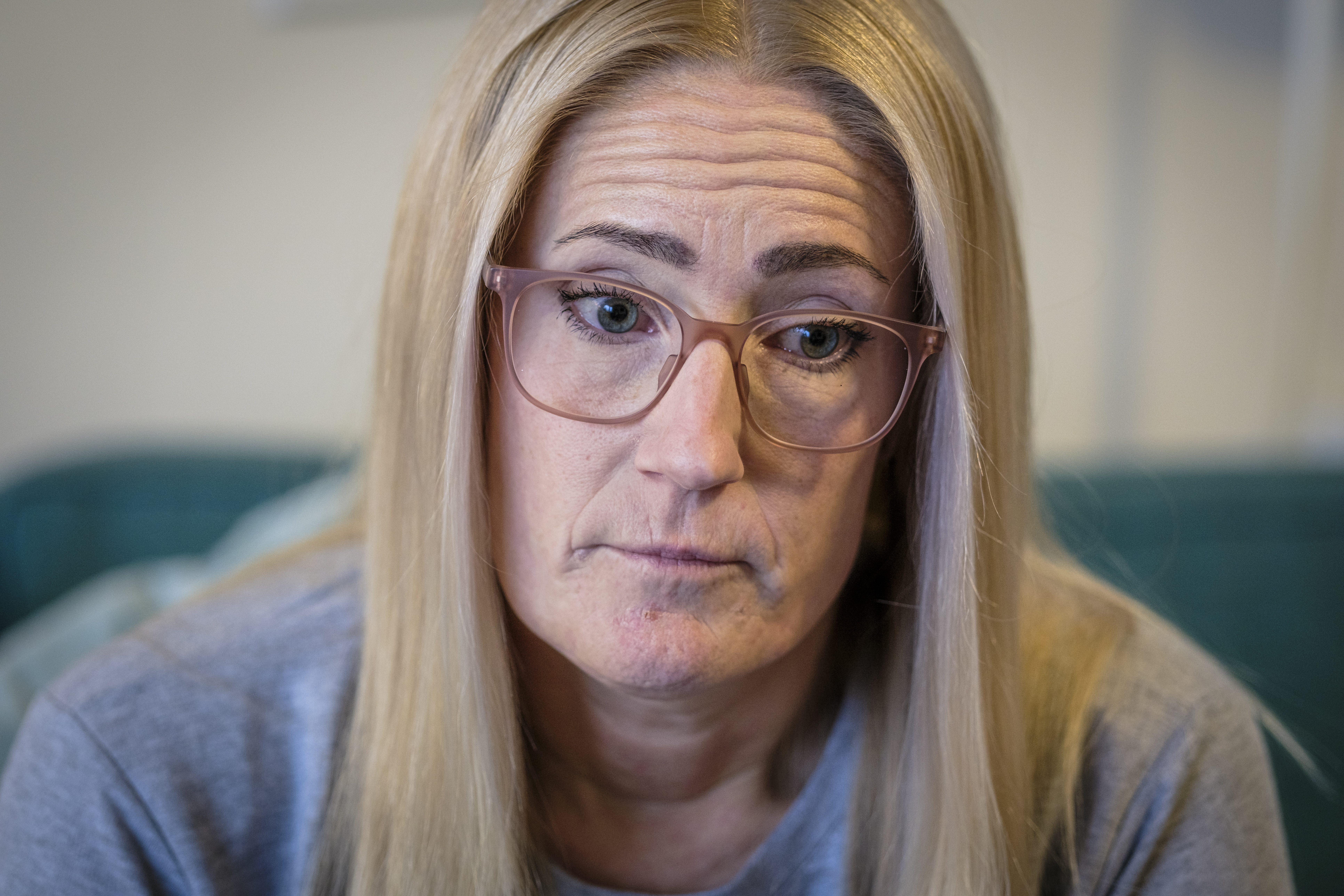 Karin Melin med långt blont hår och glasögon tittar nedåt, har en grå topp på sig och sitter inomhus.