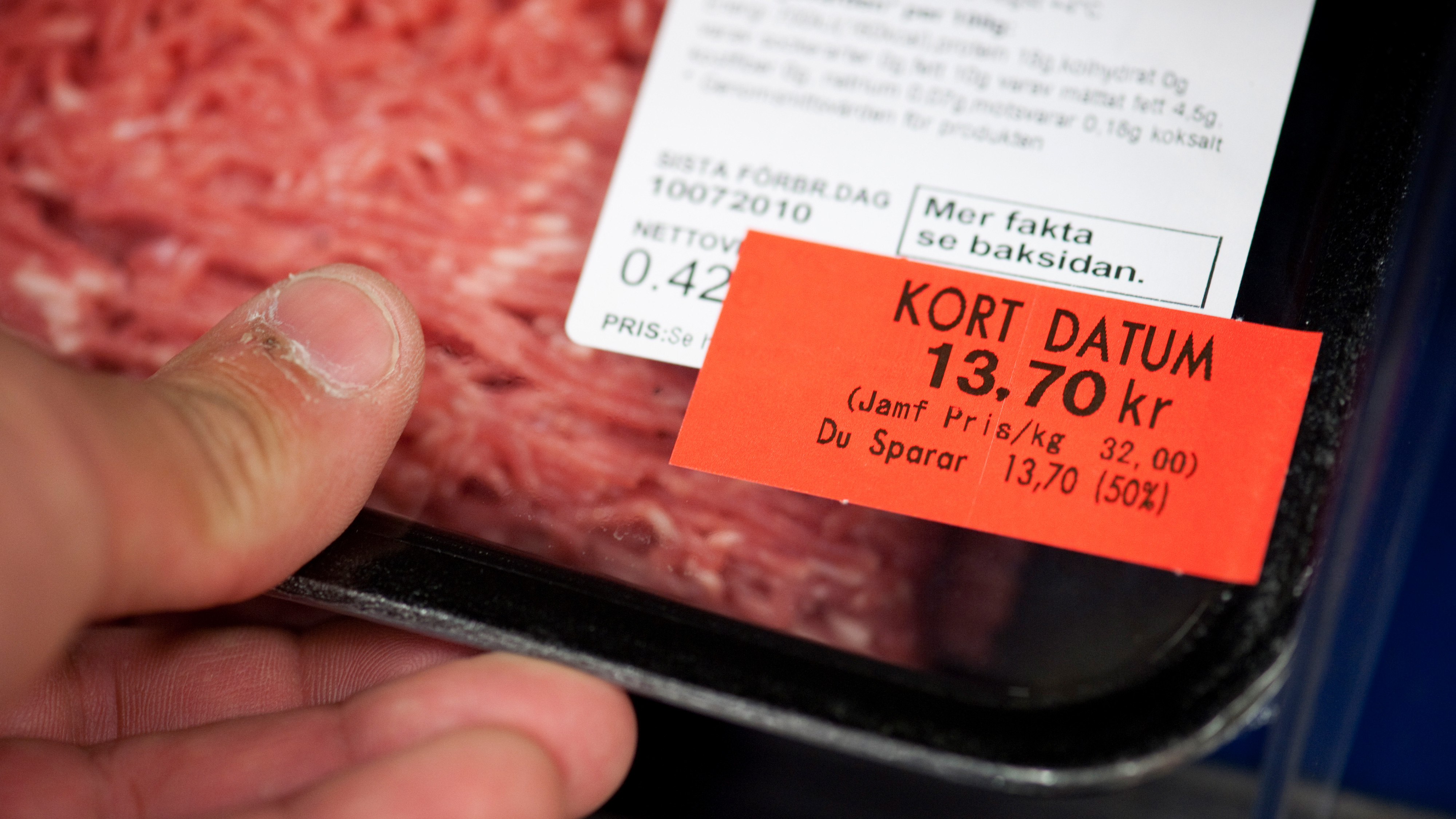 I hans hand har han en bricka med förpackad köttfärs med en röd etikett som anger det reducerade priset (13,70 svenska kronor) på grund av dess korta hållbarhet.