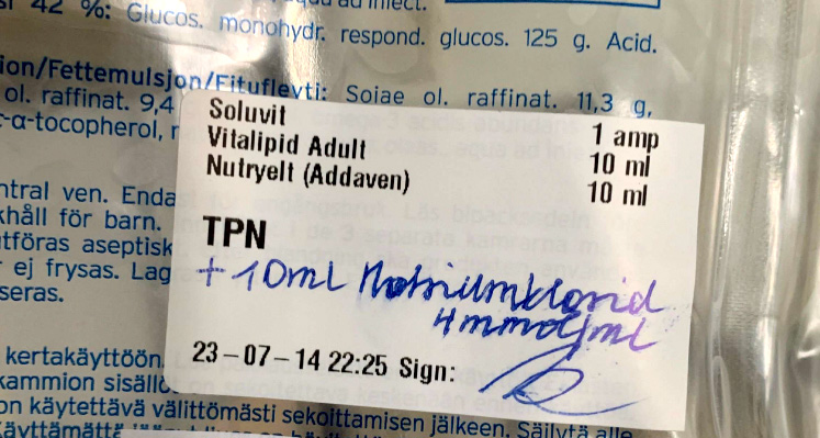 En medicinsk etikett på en droppåse visar ingredienserna Soluvit, Vitalipid Adult och Nutryelt samt handskrivna anteckningar och datum- och tidsstämpel.