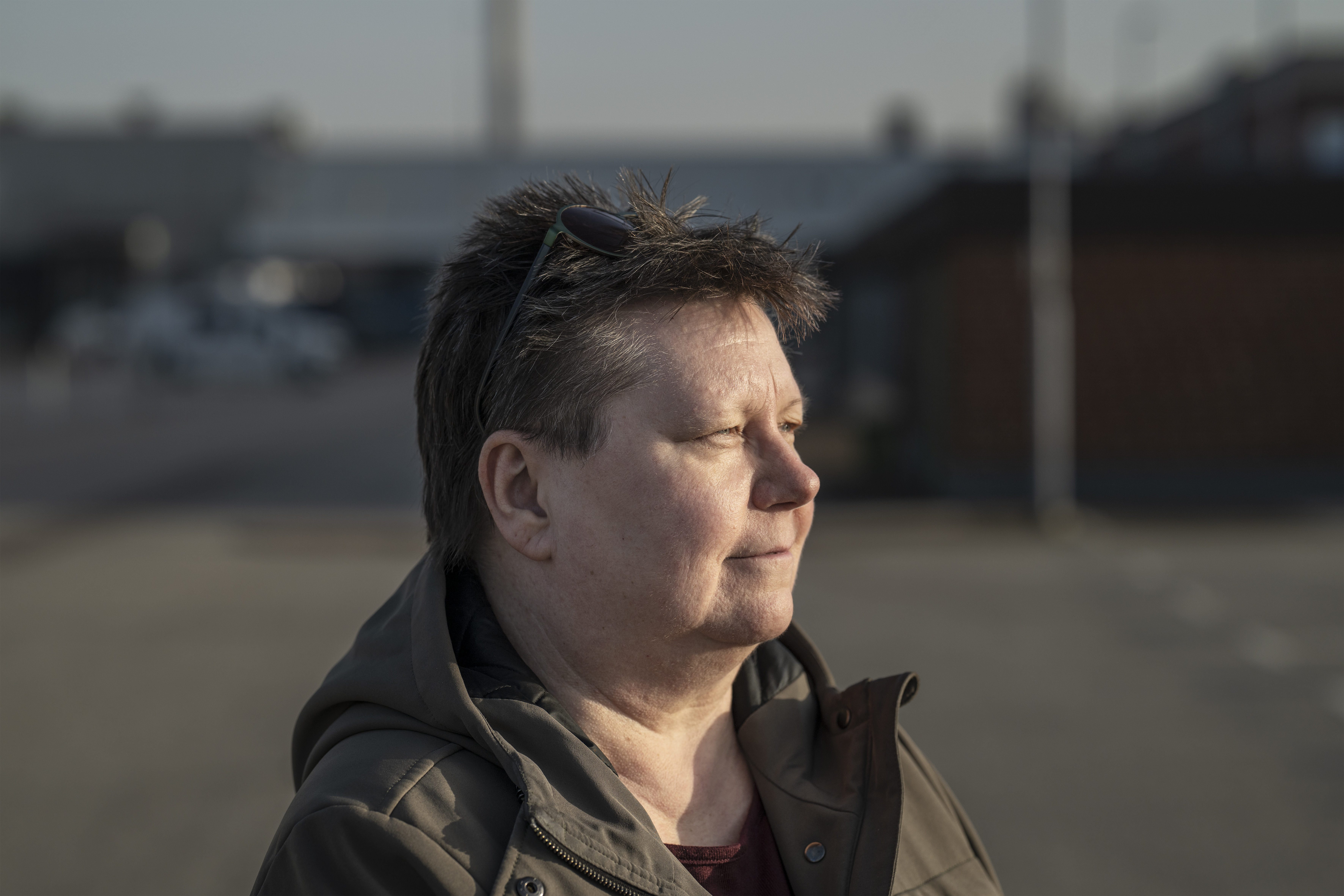 Miriam Håkansson, solglasögon på huvudet, står utanför och tittar bort, byggnader och en suddig bakgrund syns bakom henne.