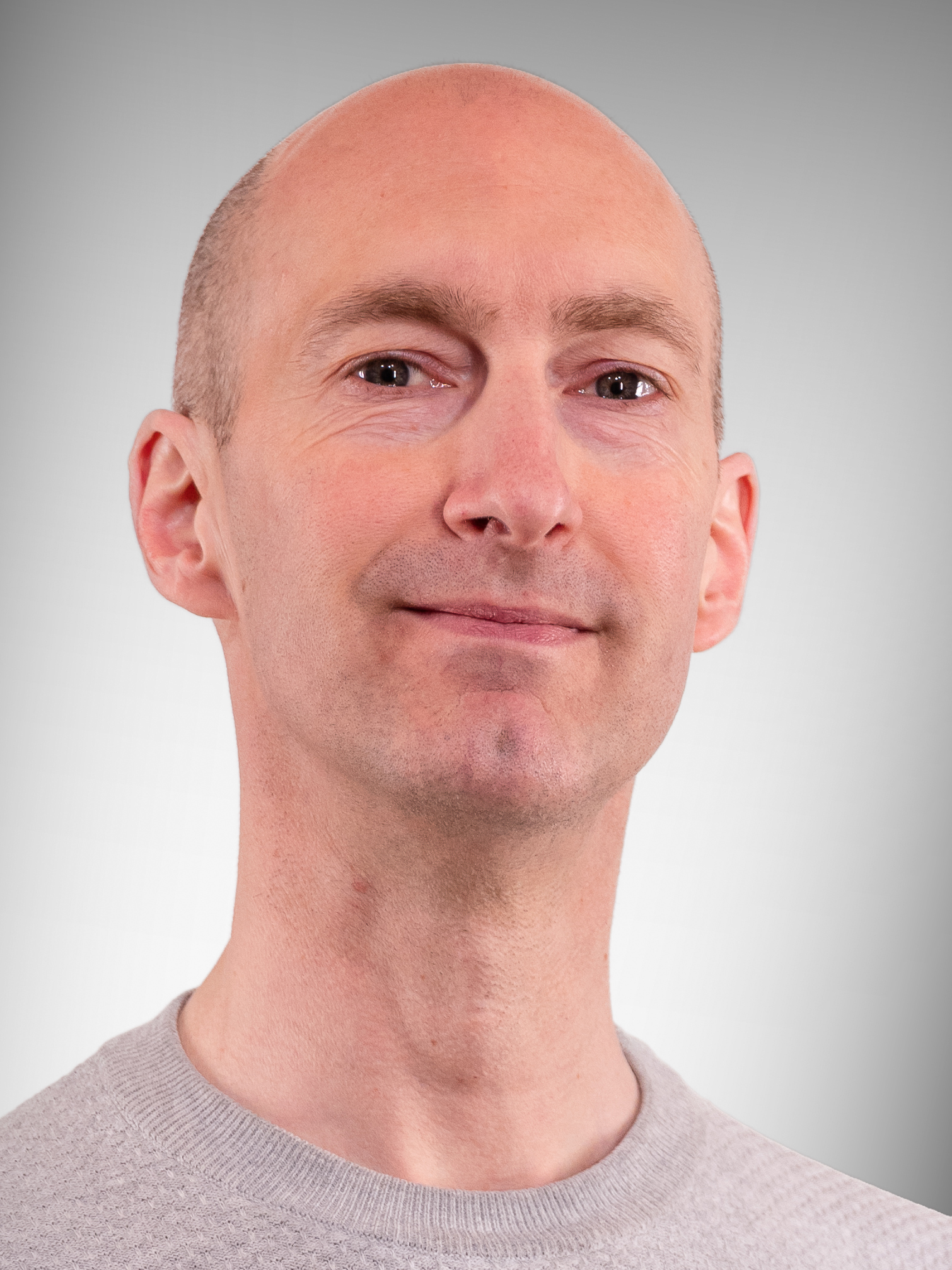 Niklas Holmqvist är klädd i en ljusgrå tröja och tittar på kameran med ett svagt leende på en grå bakgrund.