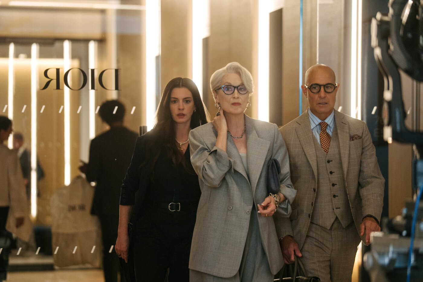Tre personer i kontorskläder går genom en hall där "DIOR" syns på en glasdörr i förgrunden.