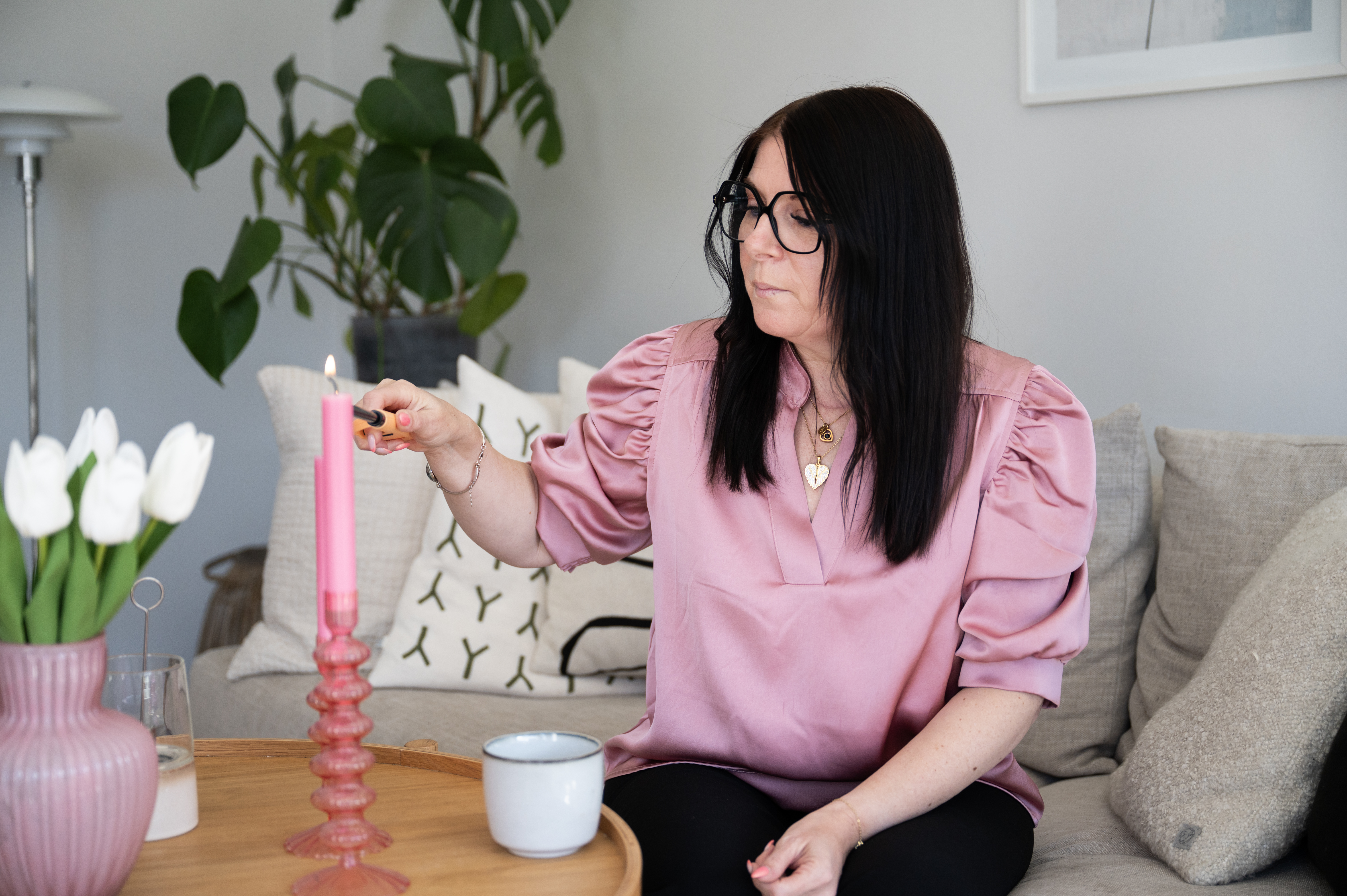 Jessica Nickel Thordsson sitter i en soffa och tänder ett rosa ljus.