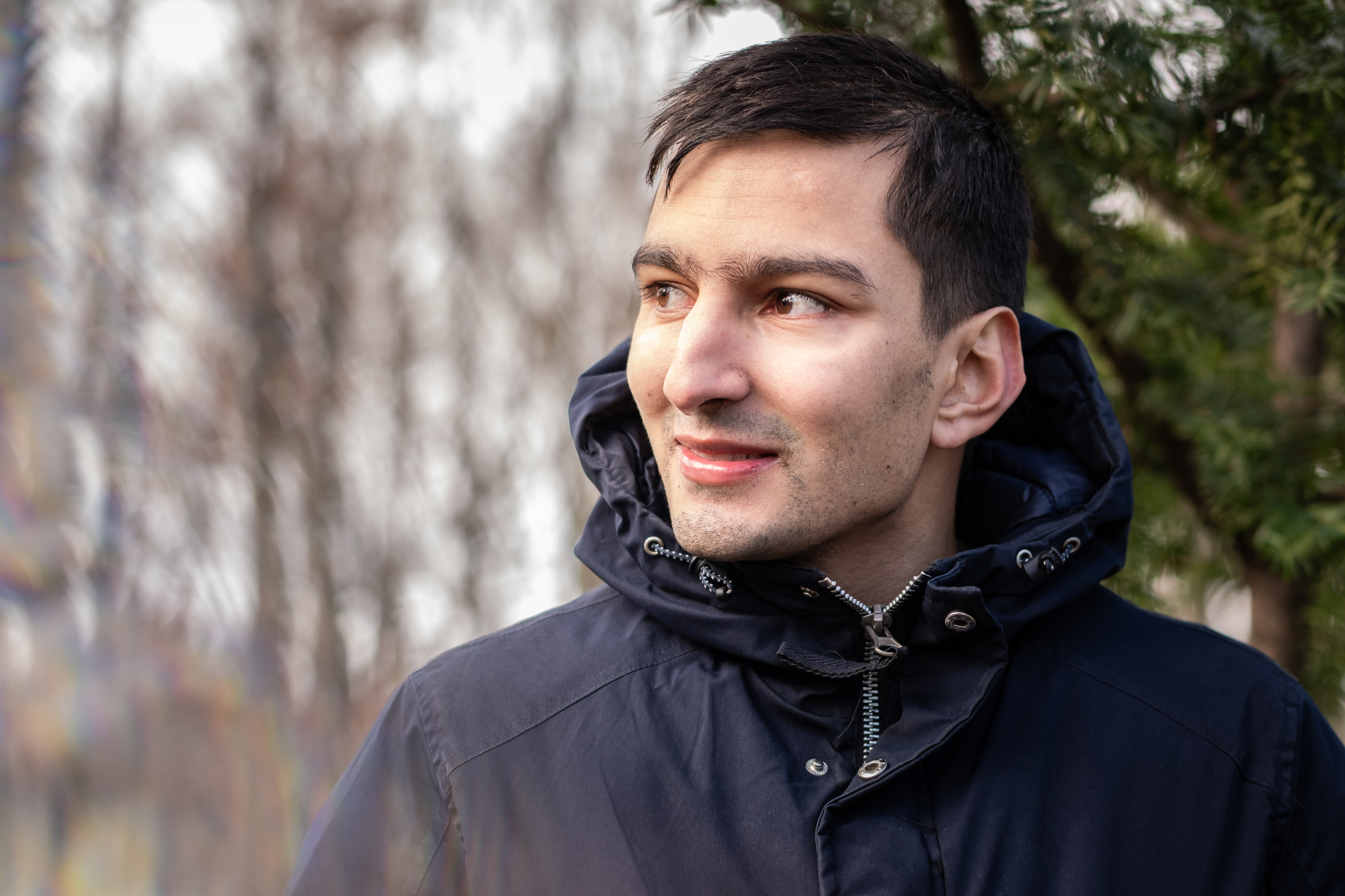 Oskar Beckström, iklädd vinterjacka, står nära växter utomhus och tittar åt sidan med ett neutralt uttryck.