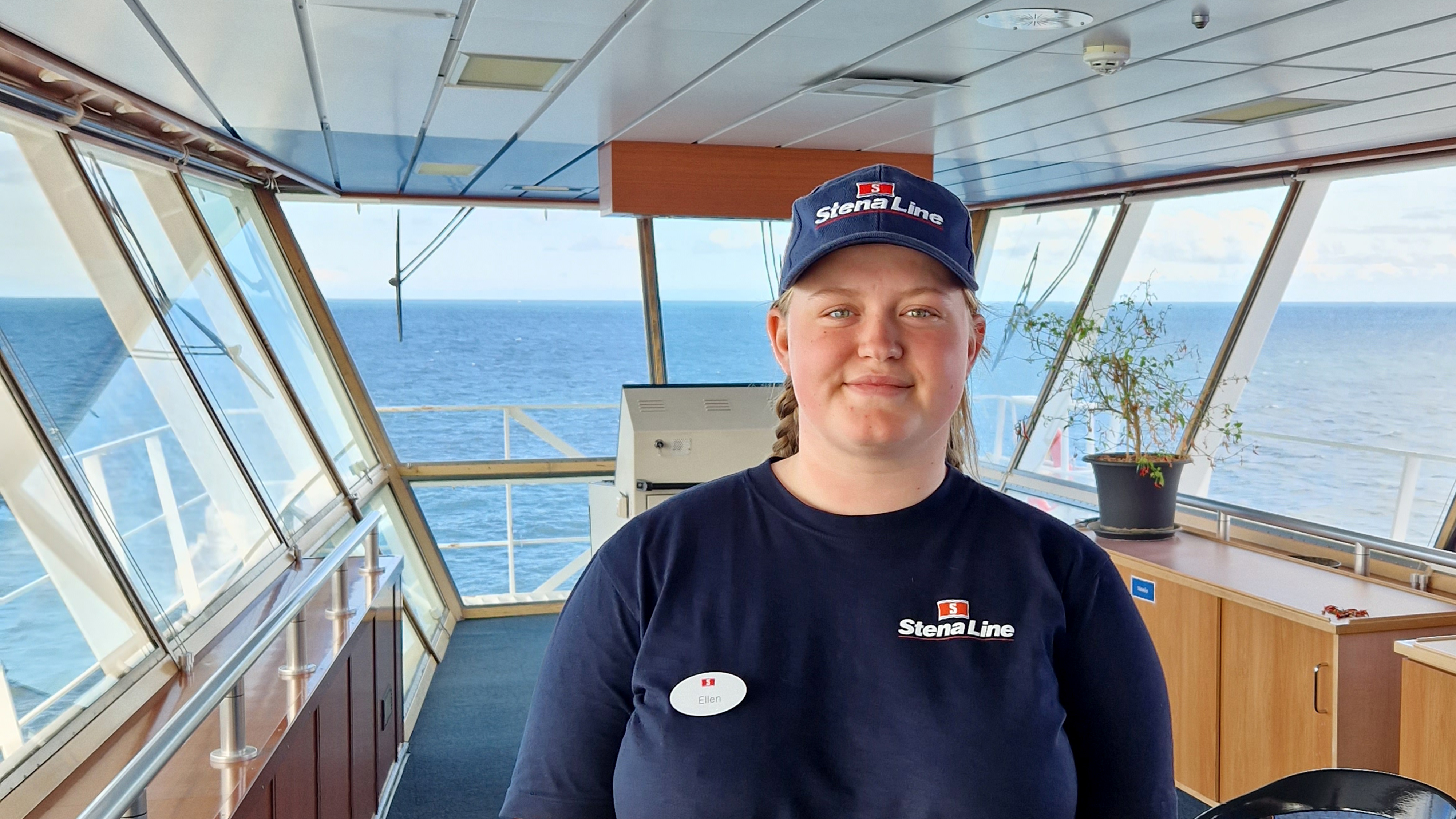 En Stena Line-besättningsmedlem i uniform står på fartygets brygga med havet synligt genom stora fönster bakom henne.