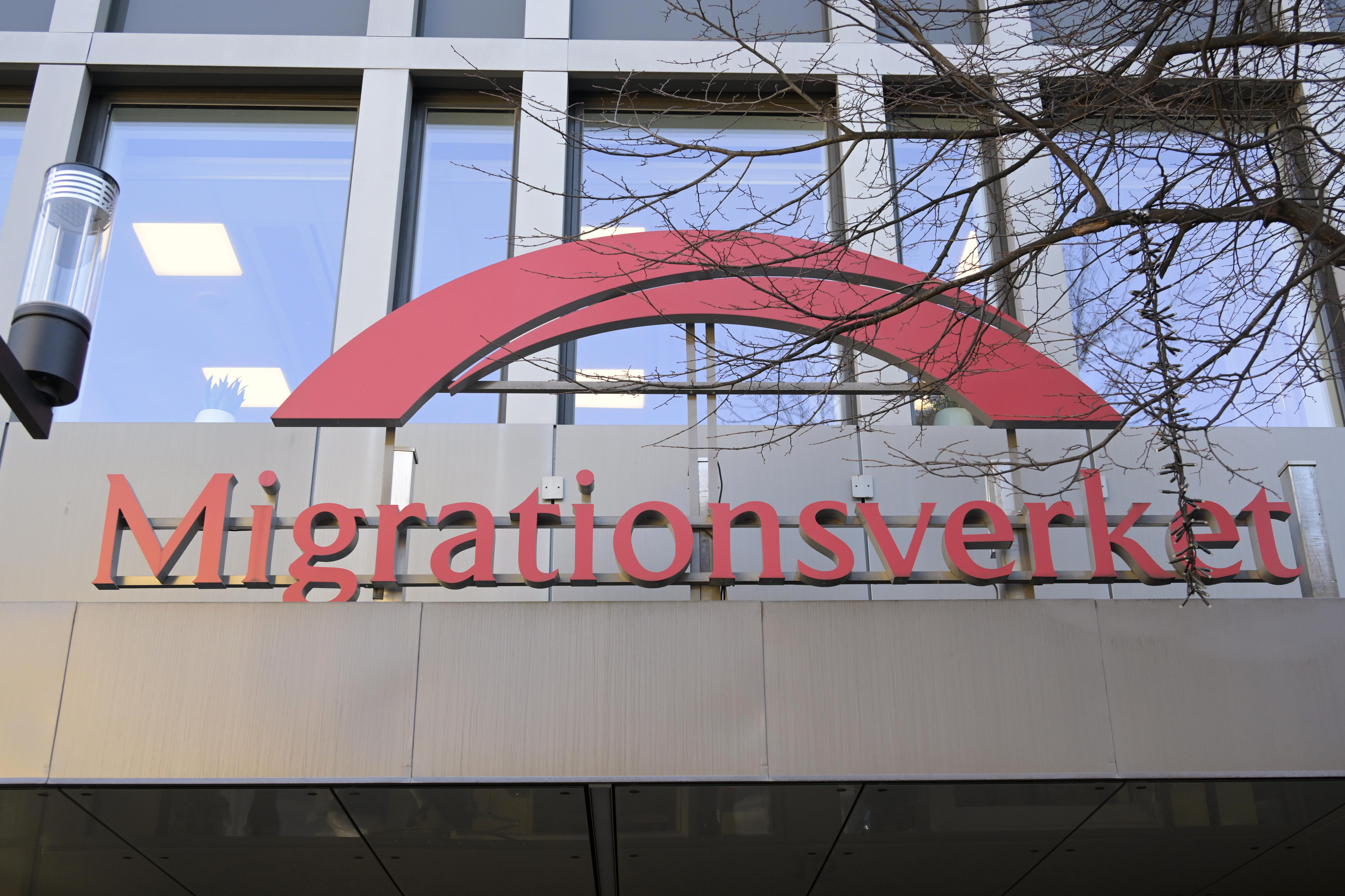 Skylt med texten ”Migrationsverket” på en fasad, med en röd båge ovanför texten.