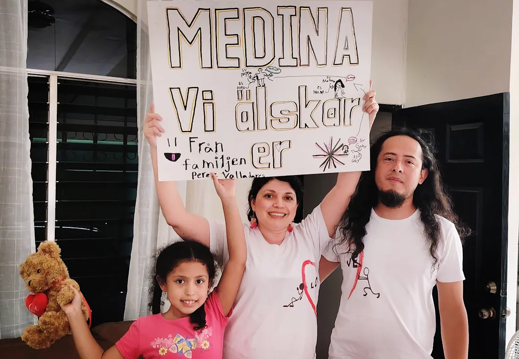 Gabby och hennes föräldrar står inne och håller i en skylt där det står