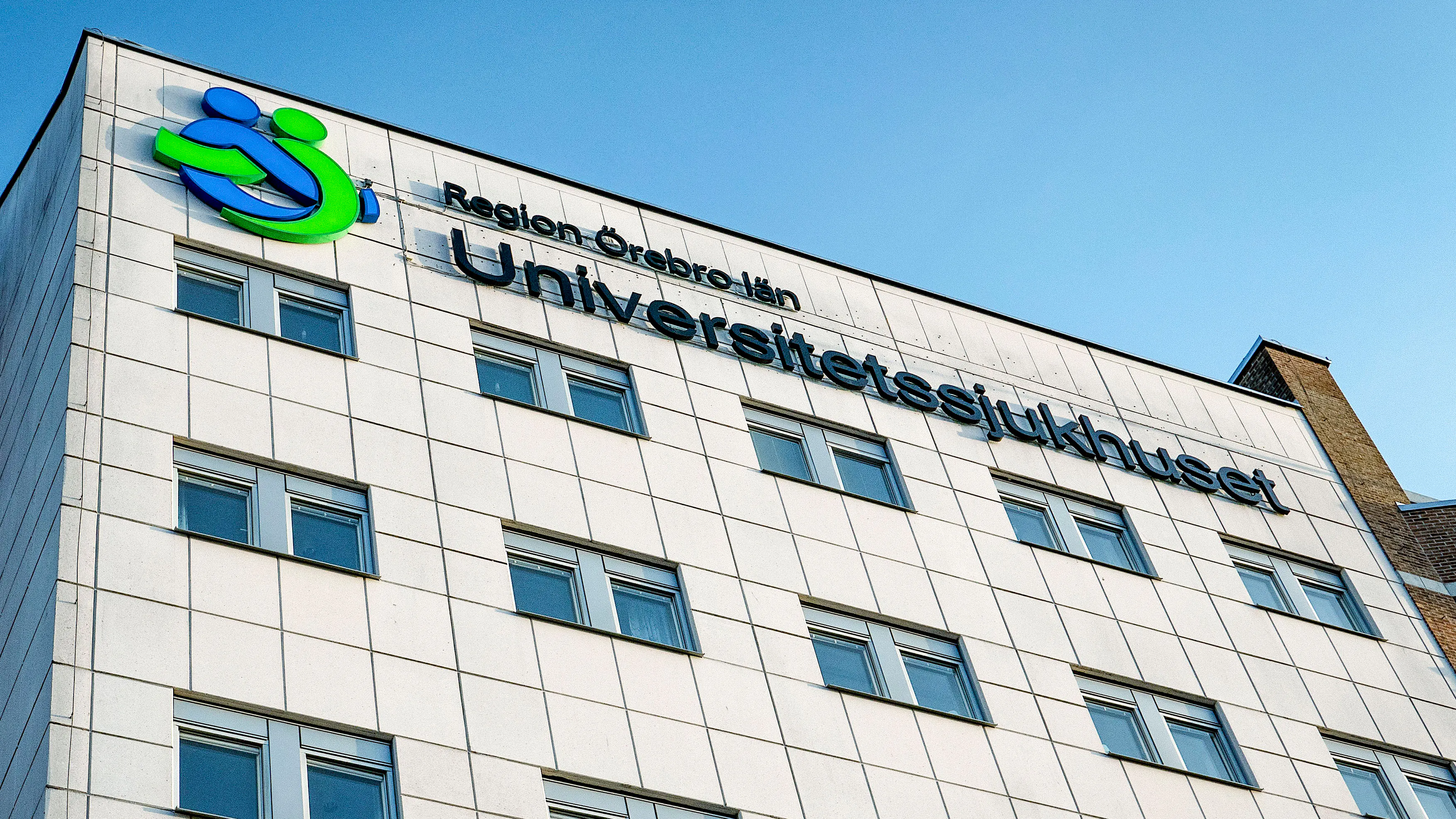 Universitetssjukhusets byggnad i Örebro, Sverige, med namn och logotyp på den övre fasaden mot en blå himmel.